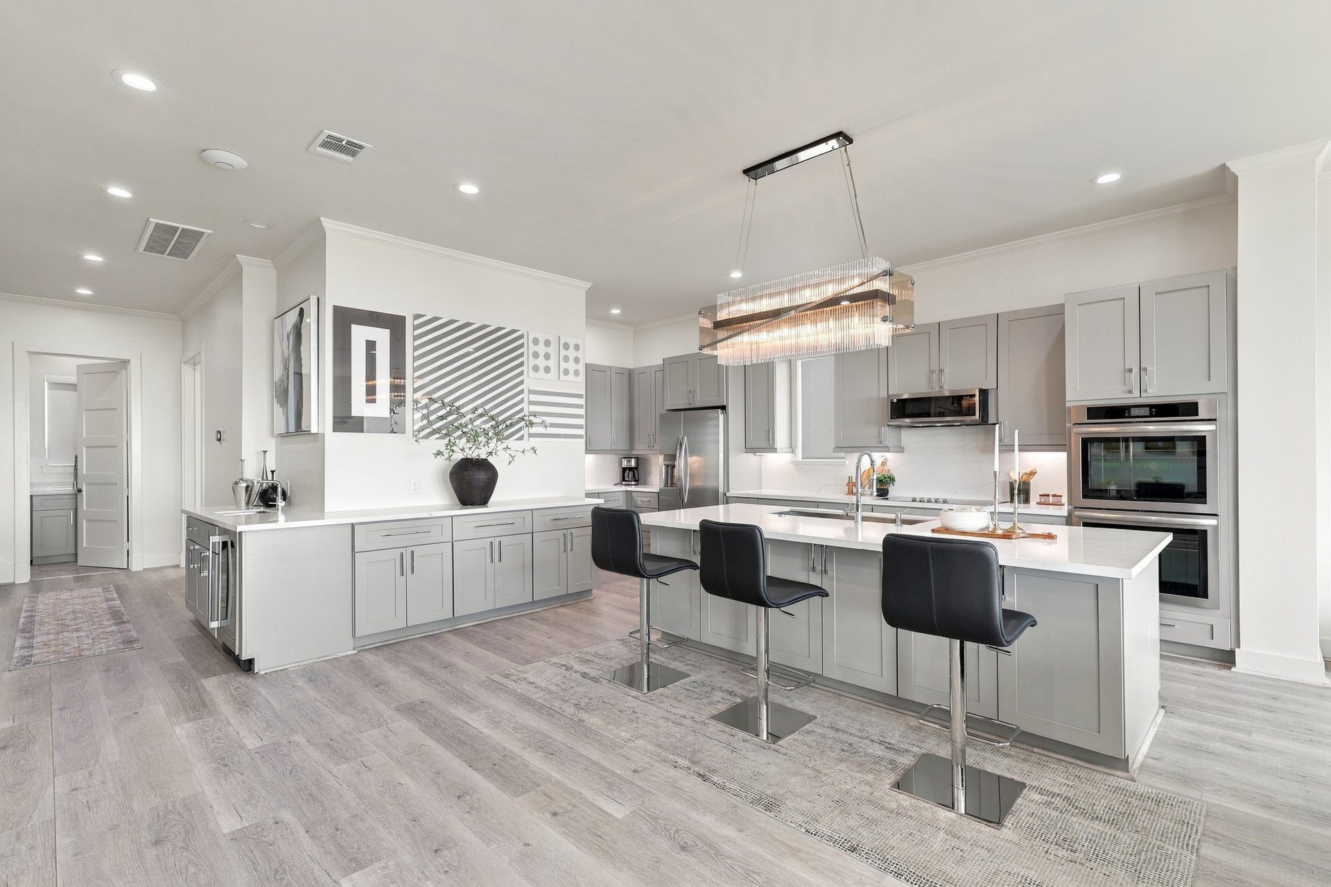 17211 Termini San Luis Pass Rd, Galveston, TX 77554 Sophisticated kitchen featuring gray cabinetry, expansive counters, stainless steel appliances, and double wall ovens. A statement chandelier highlights the oversized island with breakfast-bar seating.
