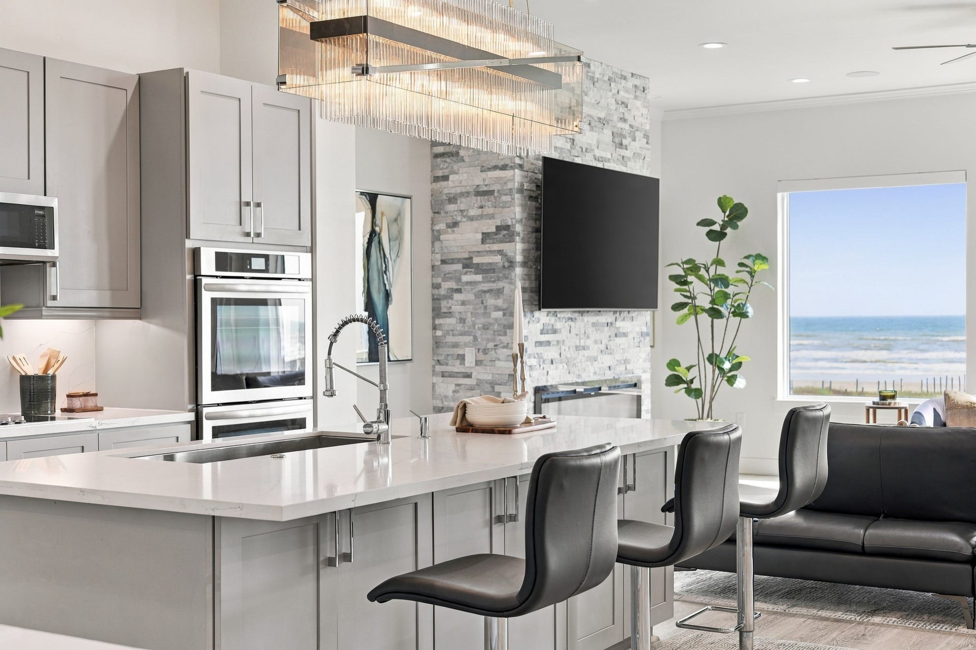 17211 Termini San Luis Pass Rd, Galveston, TX 77554 Kitchen and living detail
A generous island with breakfast-bar seating connects the kitchen to the Gulf-facing living room. Double wall ovens, gray cabinetry, and a statement chandelier balance everyday function with sophisticated style.