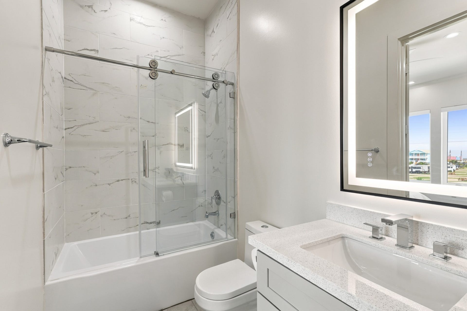 17211 Termini San Luis Pass Rd, Galveston, TX 77554 Full bathroom
Contemporary bathroom featuring a tub-and-shower combination with sliding glass doors and marble-look tile extending to the ceiling. An illuminated mirror and streamlined vanity complete the space.