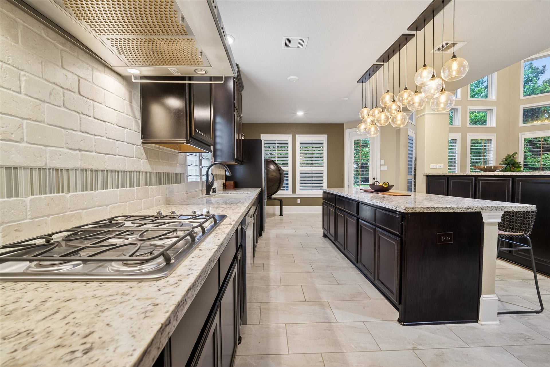 7907 Augusta Creek Court, Spring, TX 77389 Beautiful kitchen backsplash combines textured brick and glass tiles, while large windows and shutters provide plenty of natural light. Ideal for both cooking and entertaining.