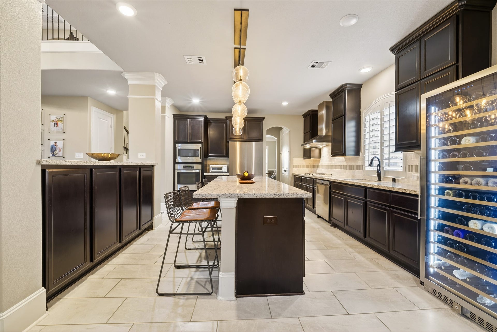 7907 Augusta Creek Court, Spring, TX 77389 This modern kitchen features dark wood cabinetry, a large central island with seating, stainless steel appliances. The space is well-lit with recessed lighting and designer inspired pendant fixtures, and offers ample counter space with a sleek, open design.