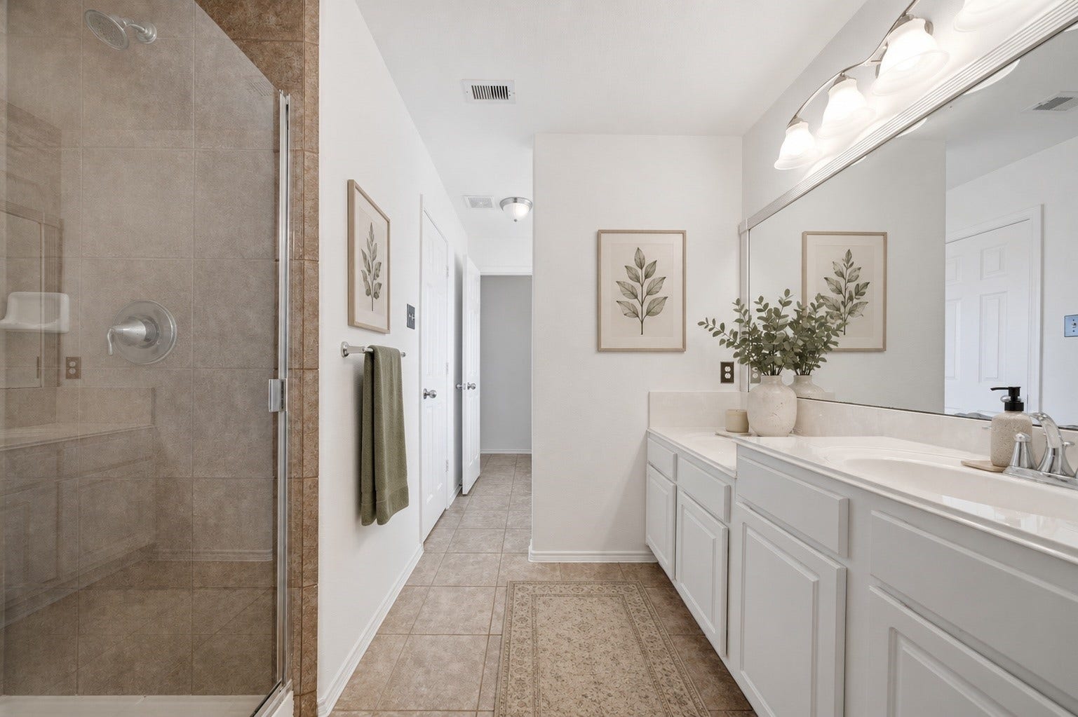 15435 Kaston Drive, Cypress, TX 77433 Crisp white vanities with dual sinks extend along tile flooring, offering ample counter space and storage beneath a large framed mirror. A glass-enclosed shower featuring neutral tile surrounds completes this spacious ensuite bath.