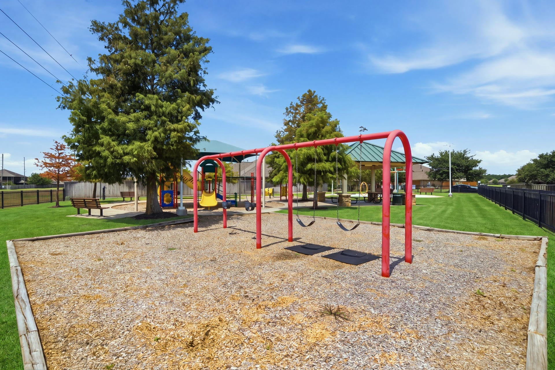 15435 Kaston Drive, Cypress, TX 77433 A red swing set anchors this neighborhood playground, featuring a wood-chip surface, swings, and a background pavilion with green space.