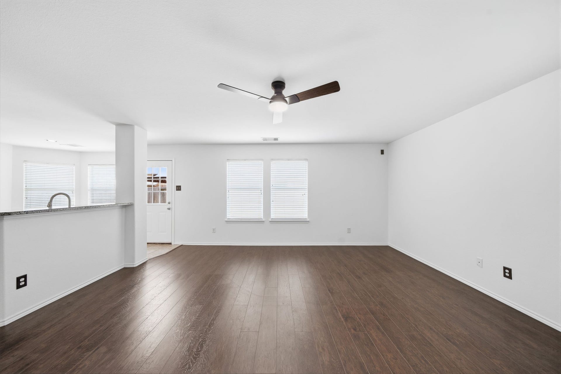 15435 Kaston Drive, Cypress, TX 77433 Gleaming dark wood-look floors span this first-floor living space, complete with a modern ceiling fan and large windows with blinds. An open wall cut-out provides a direct view into the kitchen, ensuring effortless interaction across main rooms.