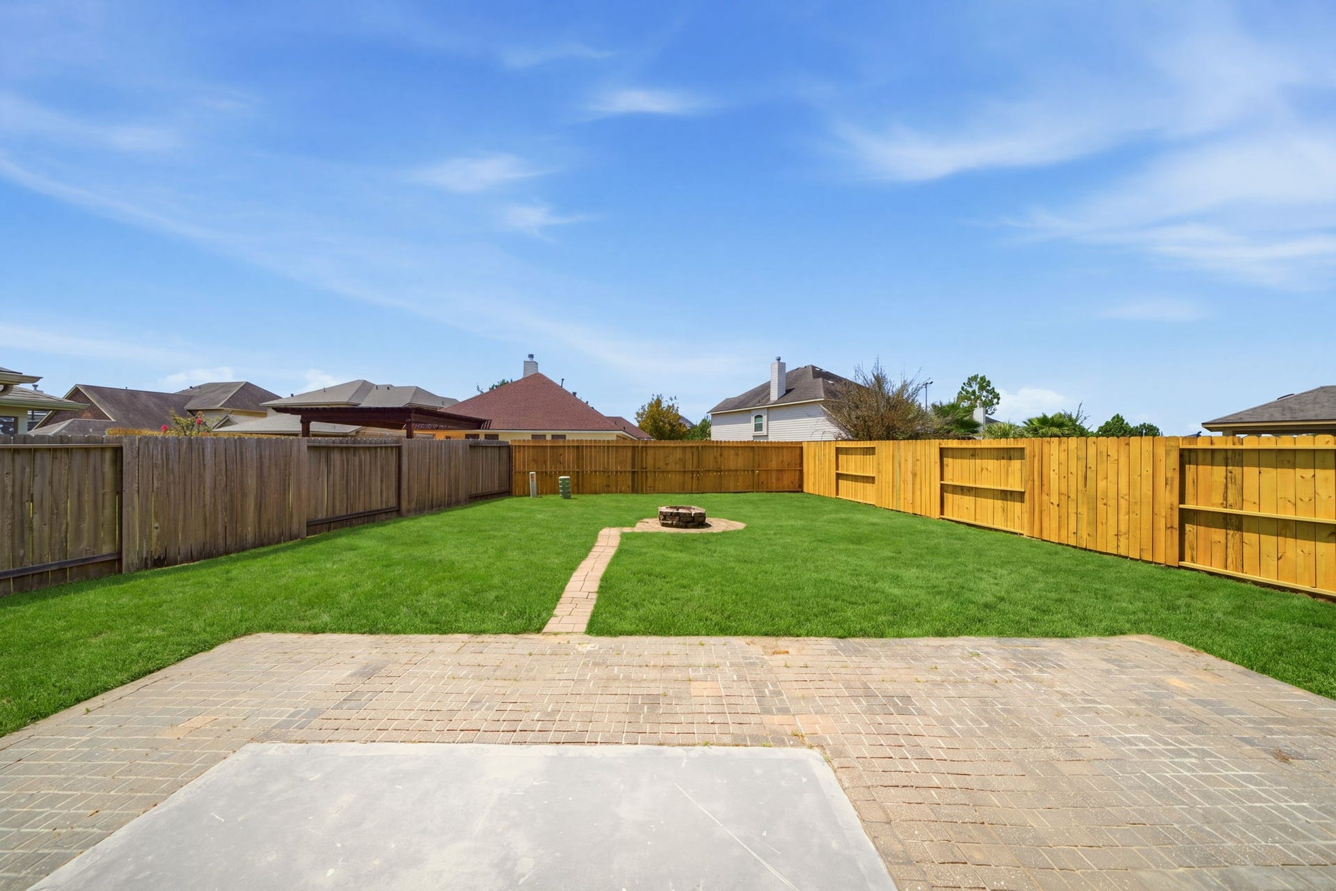 15435 Kaston Drive, Cypress, TX 77433 A brick paver patio extends into a vast green lawn within this private fenced yard, featuring a paved walkway that leads to a central fire pit. Plenty of open space provides endless possibilities for a custom pool or a lush garden setup.