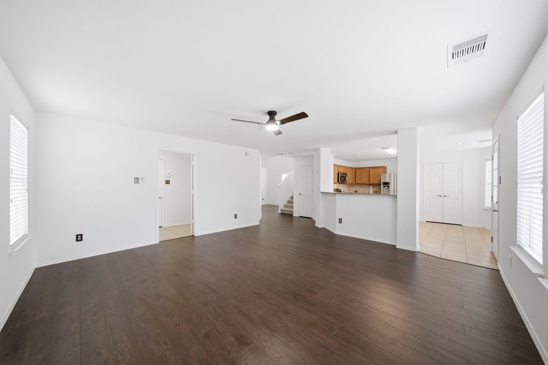 15435 Kaston Drive, Cypress, TX 77433 Rich dark hardwood floors and crisp white walls frame this spacious first-floor living area featuring a central ceiling fan. An open layout connects the space directly to the kitchen's breakfast bar, while wide windows provide ample light.