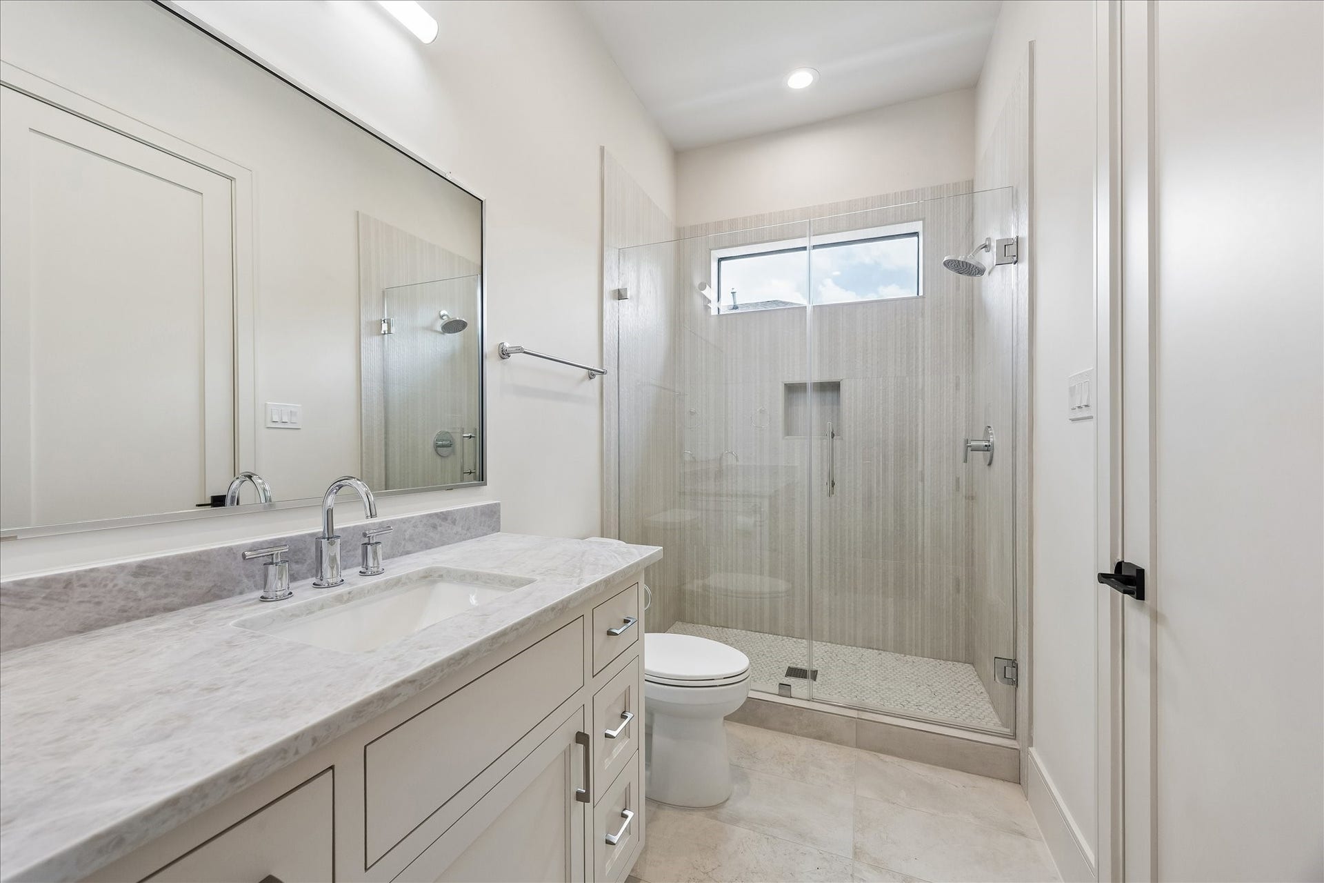 316 W 30th Street, Houston, TX 77018 Soft neutral finishes, a quartz vanity, and a frameless glass shower create a timeless ensuite bath. Full height tile, a built in shower niche, and transom window add both style and natural light.
