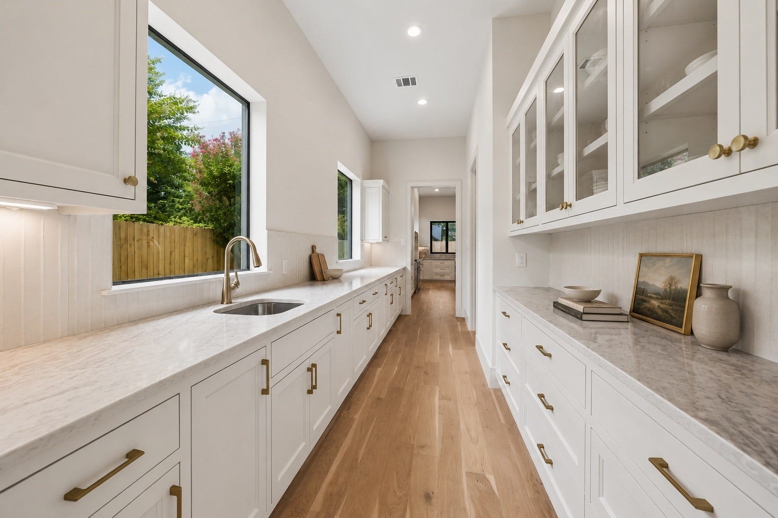 316 W 30th Street, Houston, TX 77018 Prep work feels elevated in a massive scullery with extensive cabinetry, a large walk in pantry for dry goods, and a secondary sink tucked beneath a large picture window - already plumbed and ready for a dishwasher install. Glass front uppers, natural stone surfaces, and thoughtfully curated finishes create a clean extension of the main kitchen while keeping everyday essentials organized and out of sight. **Virtually staged**