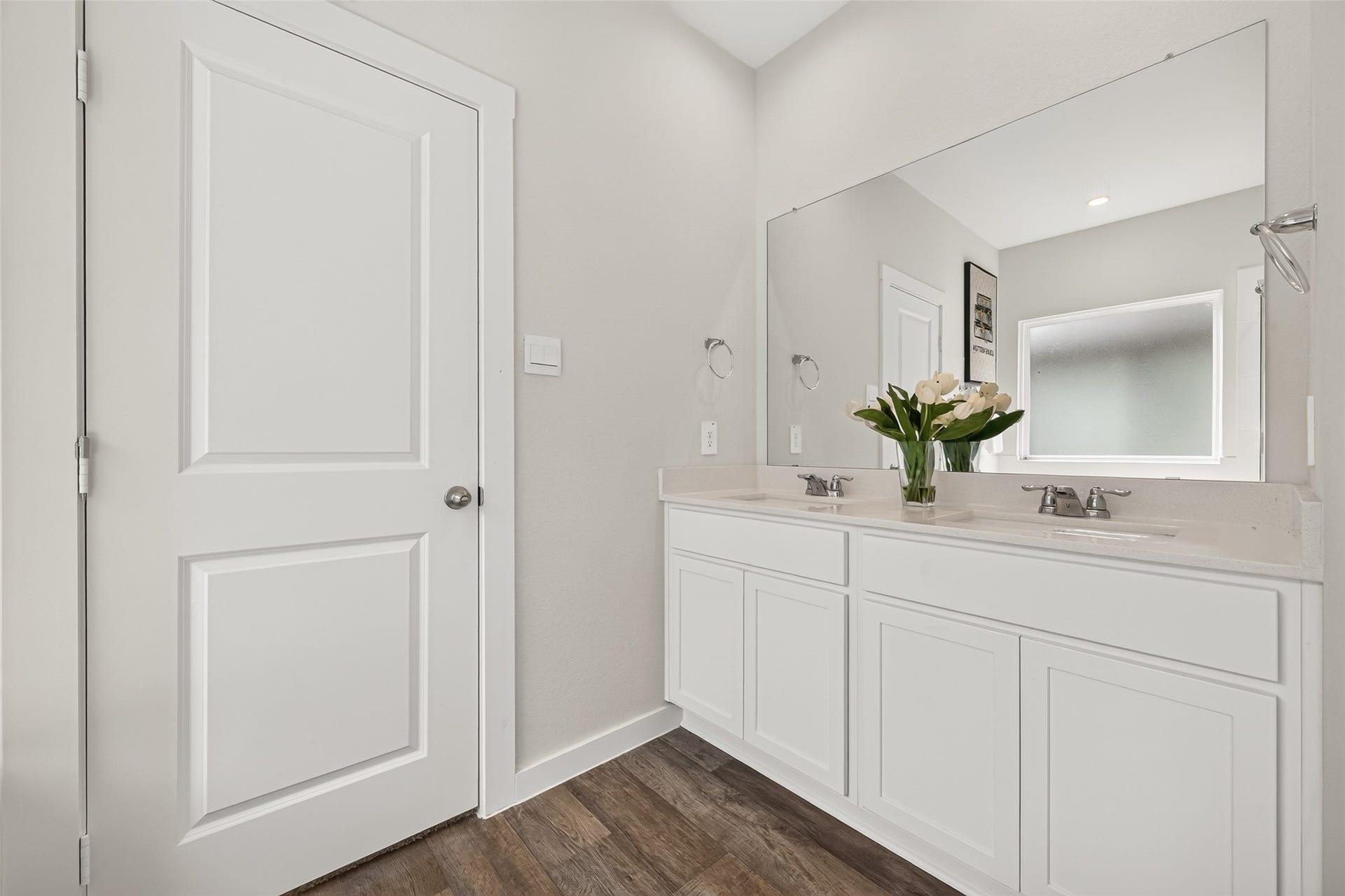 Bright and modern bathroom featuring a double vanity with sleek white cabinetry, complemented by a large mirror and elegant wood flooring.