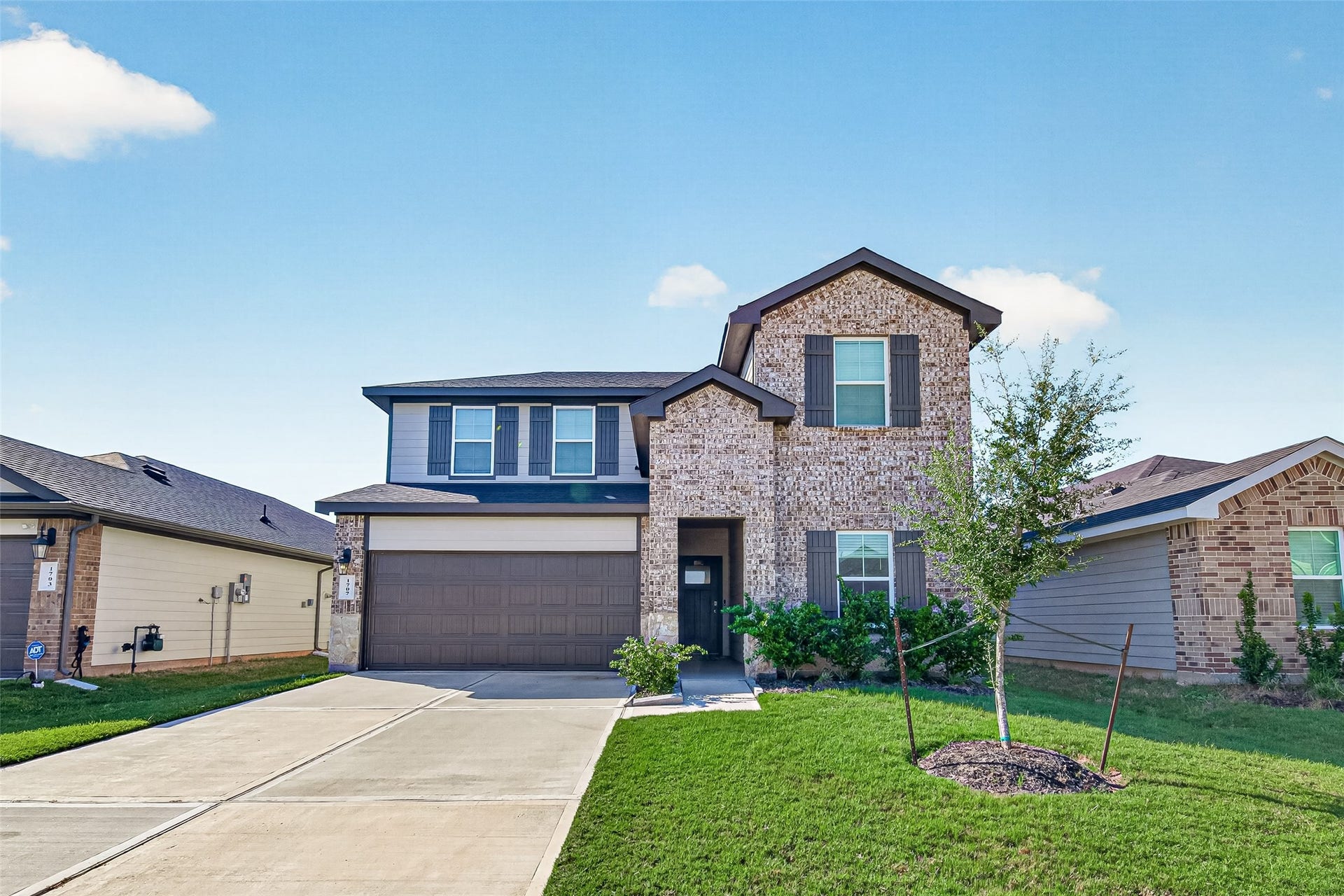 Charming two-story home with a brick exterior, featuring a welcoming front lawn and a spacious two-car garage.
