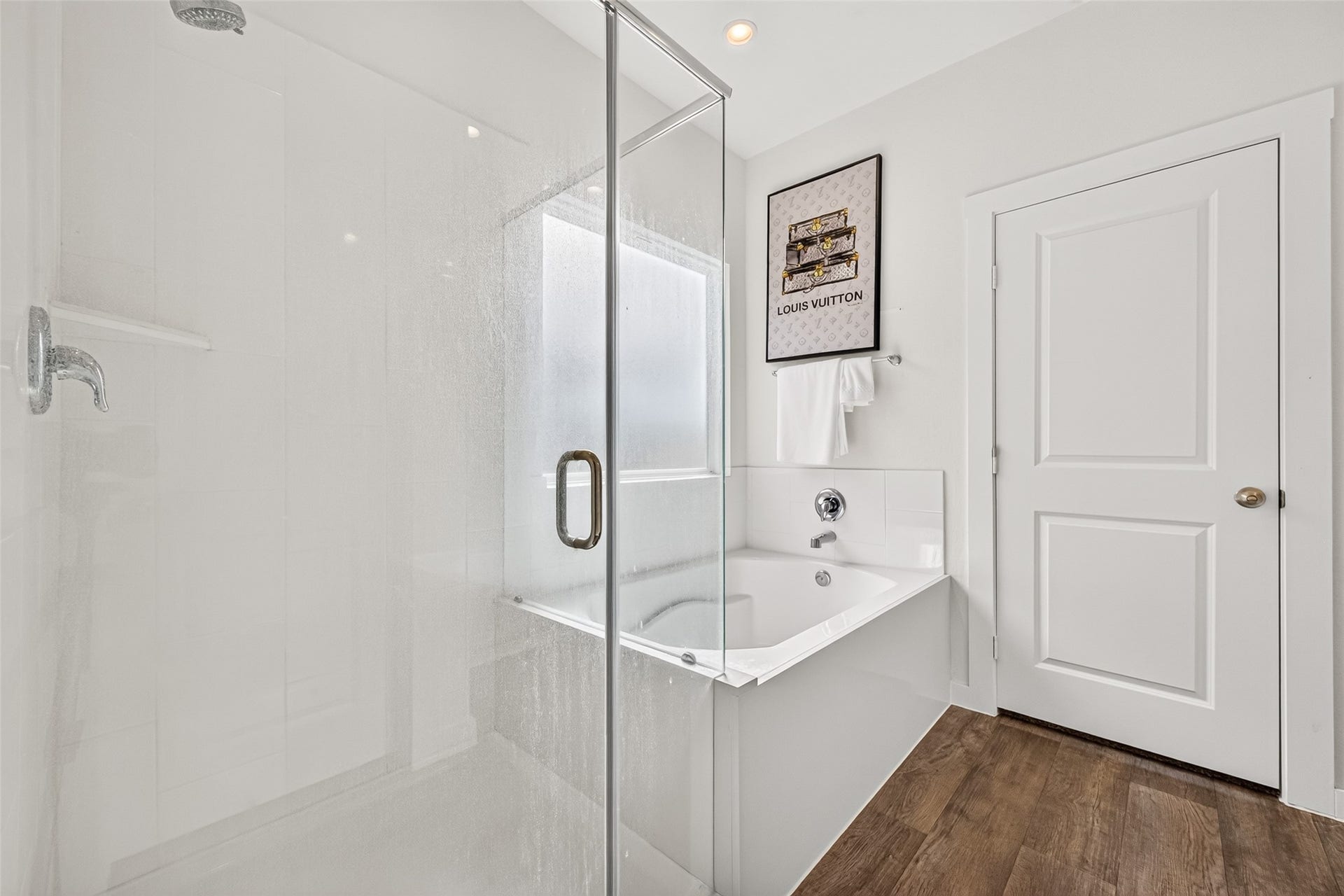 Bright and modern bathroom featuring a sleek glass-enclosed shower and a spacious soaking tub, complemented by elegant wood-style flooring.