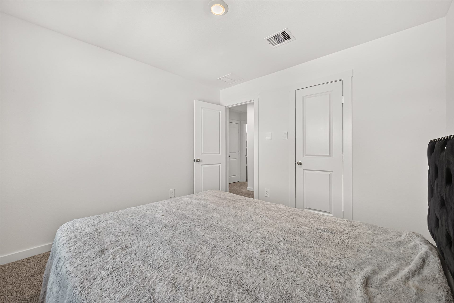 Cozy bedroom with plush carpeting, a comfortable bed, and ample natural light from the hallway.
