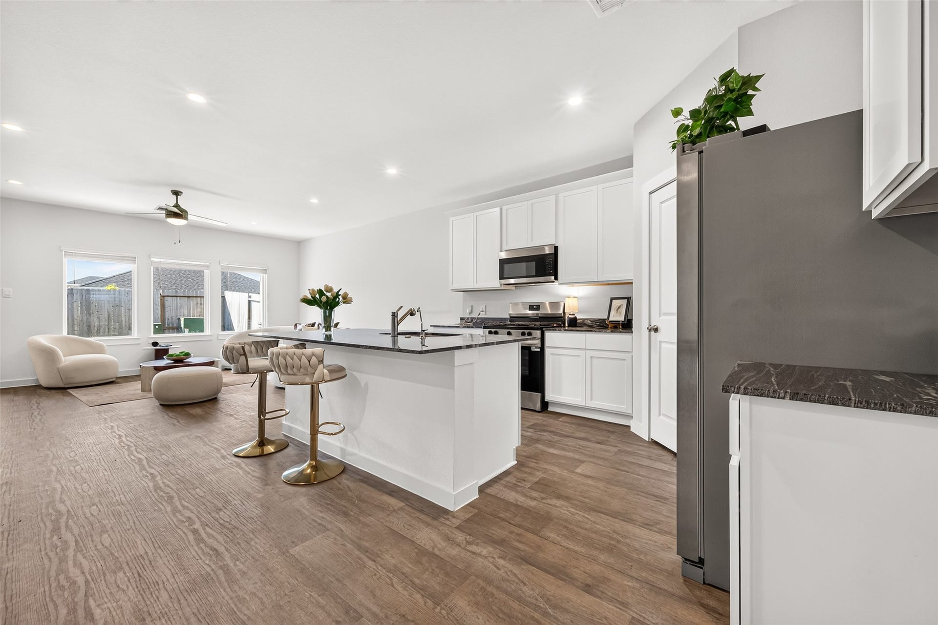 Bright and open kitchen and living area featuring sleek white cabinetry, modern appliances, and a spacious island with seating. The adjoining living space offers ample natural light and stylish, comfortable furnishings.