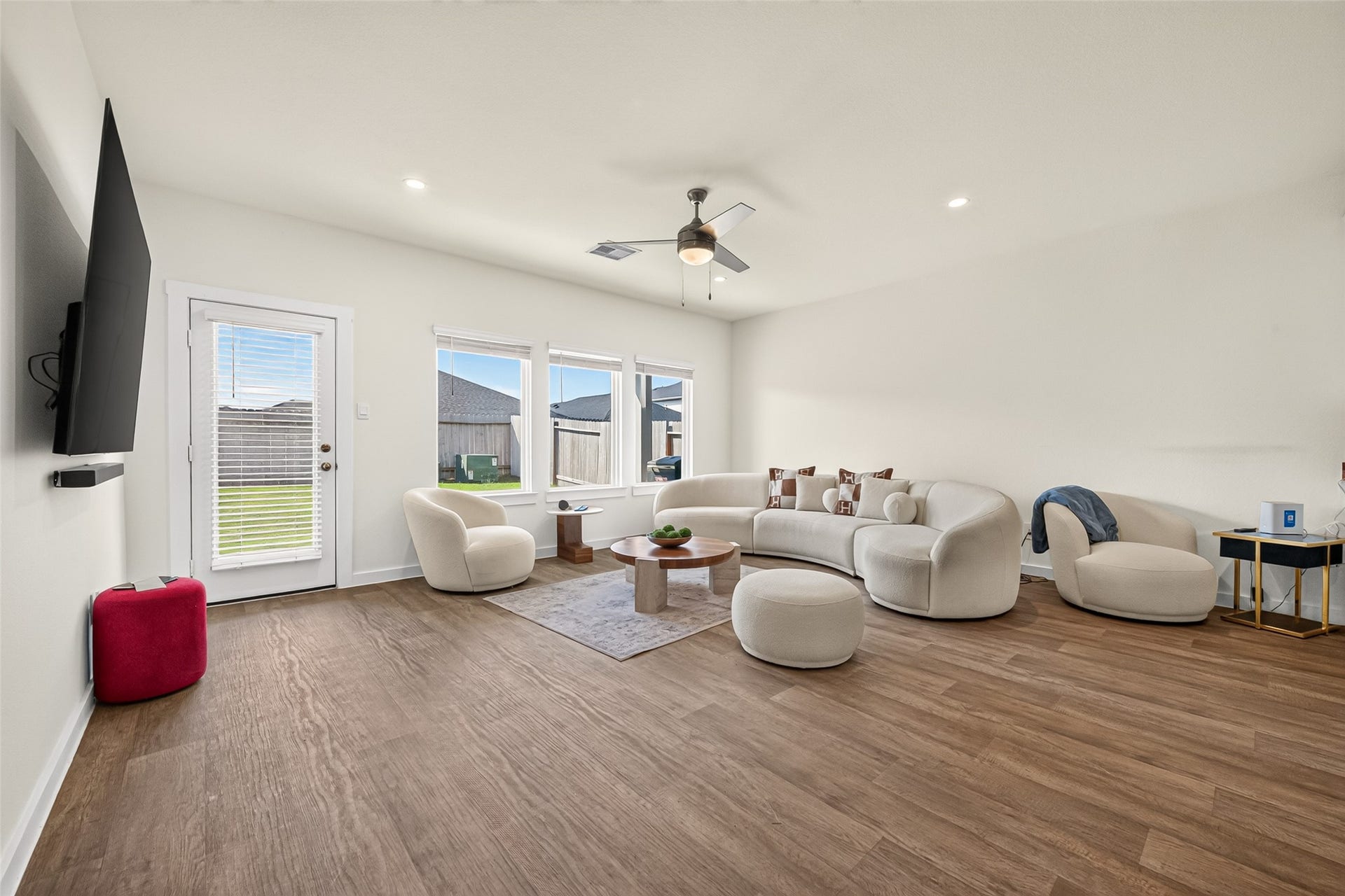 Spacious living room with elegant hardwood floors, a cozy curved sofa, and abundant natural light from large windows, perfect for relaxation and entertaining.
