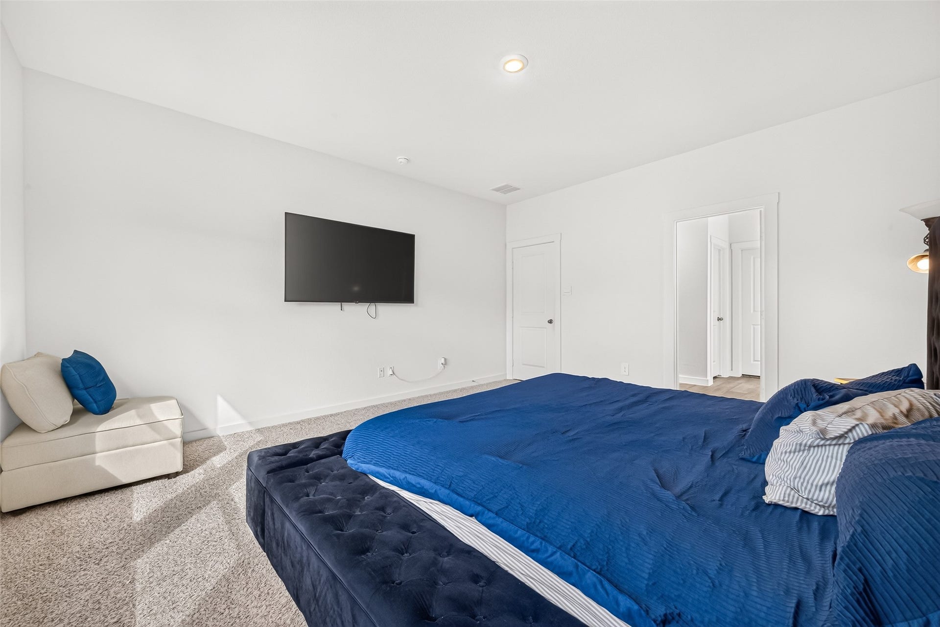 Spacious bedroom featuring a plush bed, wall-mounted TV, and soft carpeting, offering a comfortable and inviting retreat.