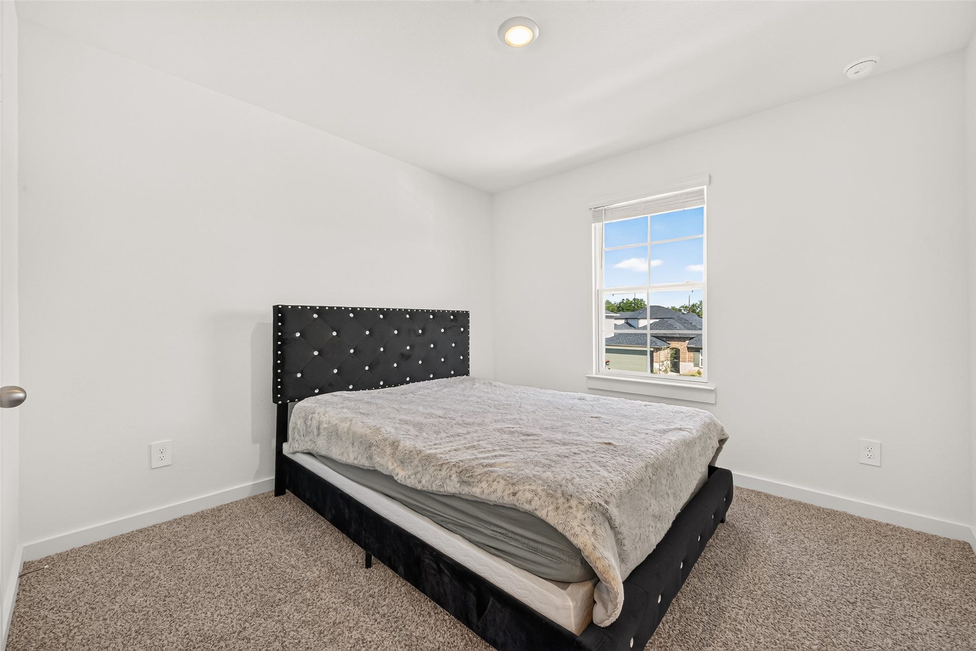 Cozy bedroom with a plush carpet, large window for natural light, and a stylish upholstered bed frame.