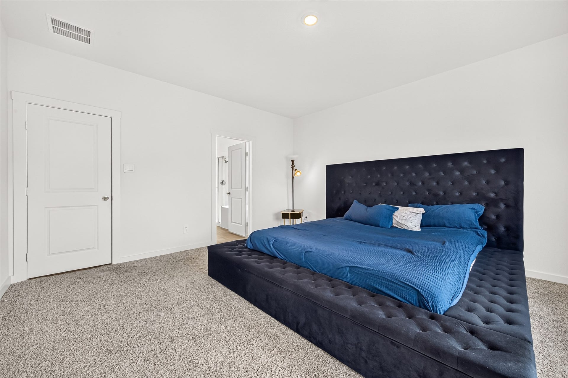 Spacious bedroom featuring a luxurious tufted bed with plush carpeting and soft, neutral walls.