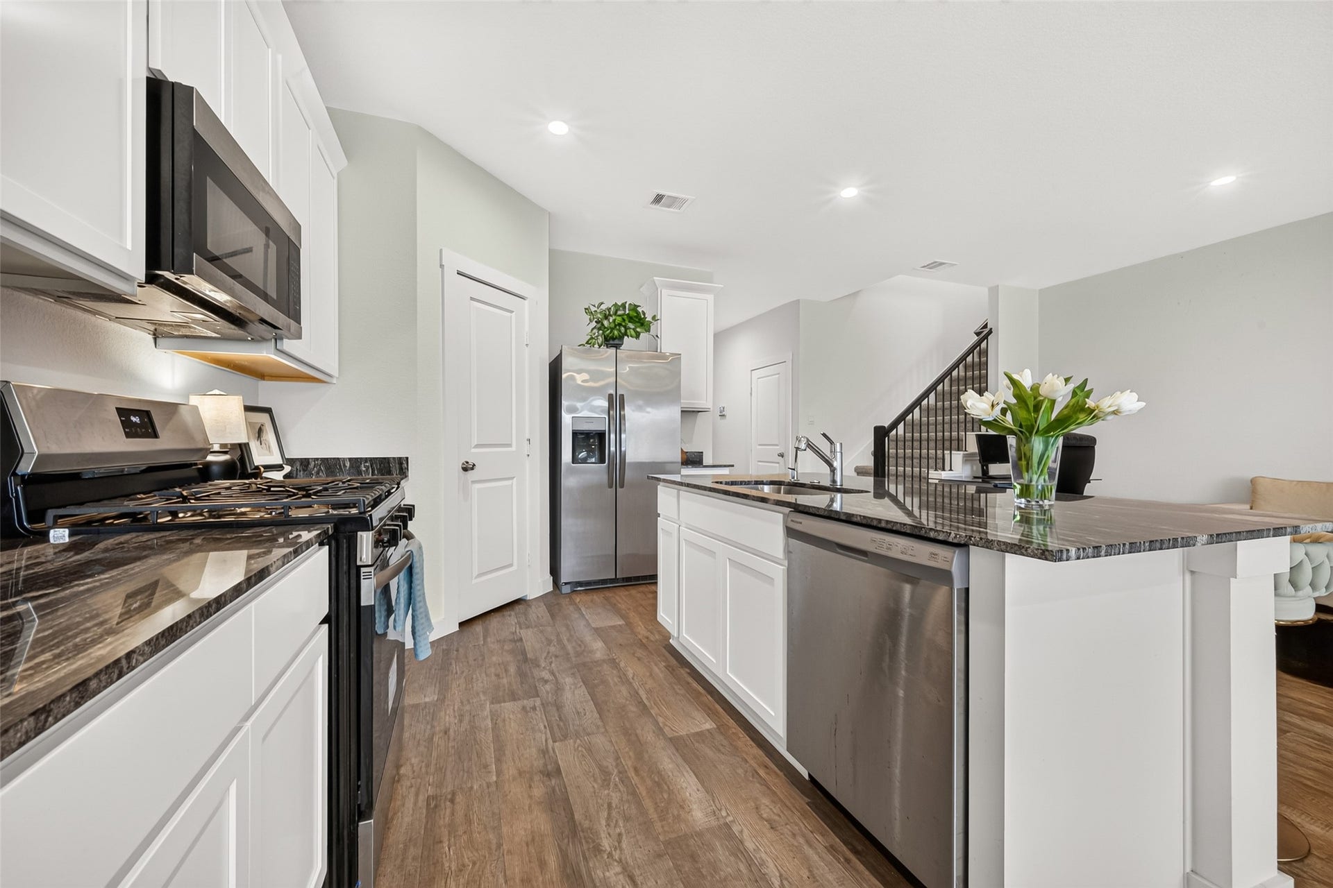 Modern kitchen featuring sleek granite countertops, stainless steel appliances, and a spacious island with bar seating, complemented by elegant wood flooring and recessed lighting.