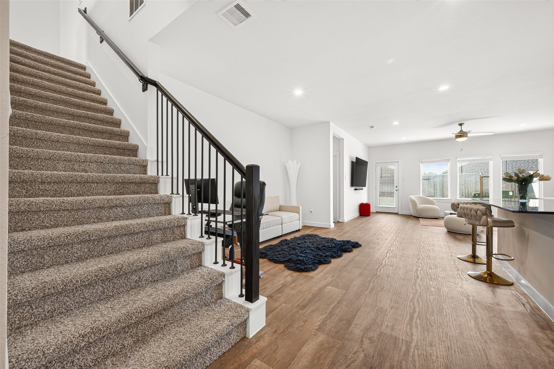 Spacious open-concept living area with elegant wood flooring, modern fixtures, and abundant natural light, seamlessly connected to a cozy carpeted staircase.