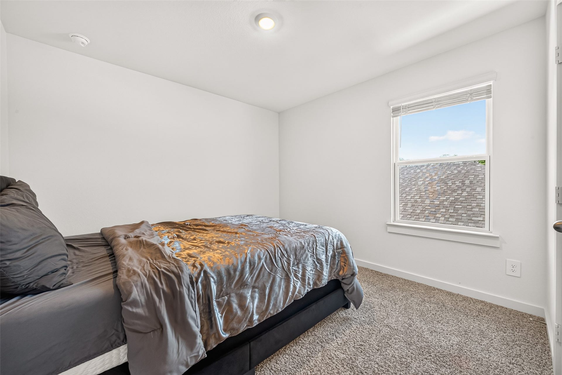 Cozy bedroom with plush carpeting, a soft bedspread, and a bright window offering natural light.