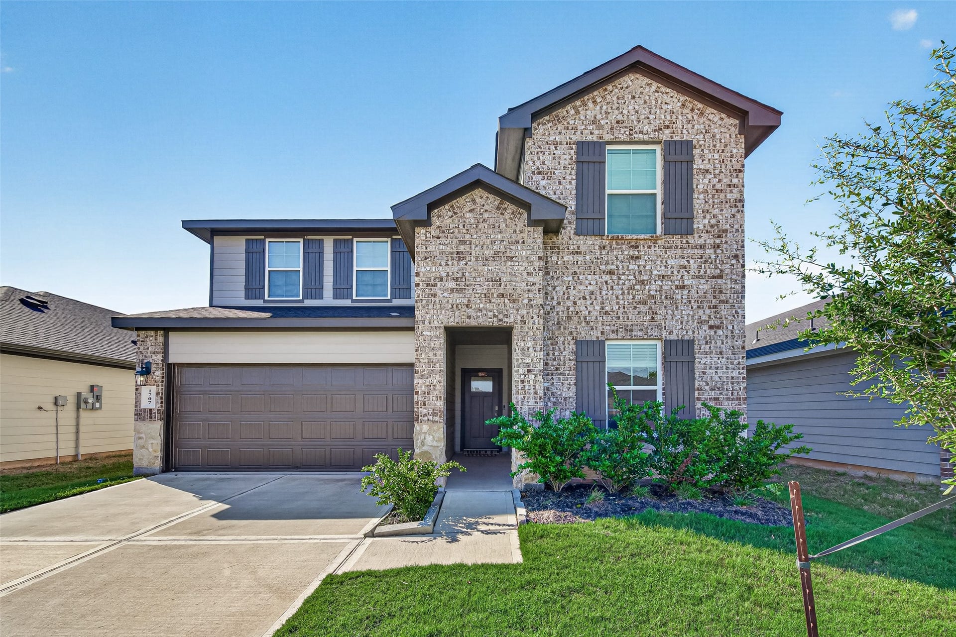 Charming two-story brick home with modern accents, featuring a spacious two-car garage and neatly landscaped front yard.