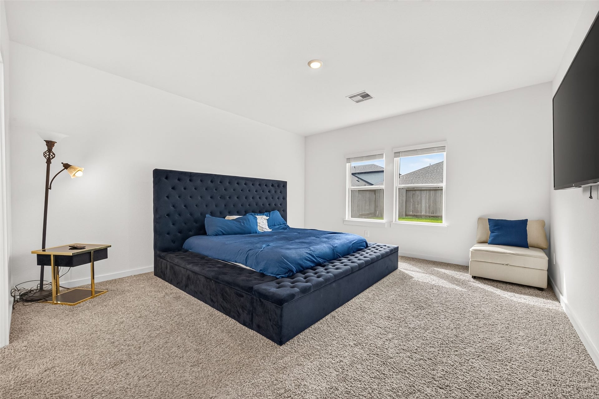 Spacious bedroom featuring a plush, tufted bed frame, large windows for natural light, and cozy carpet flooring.