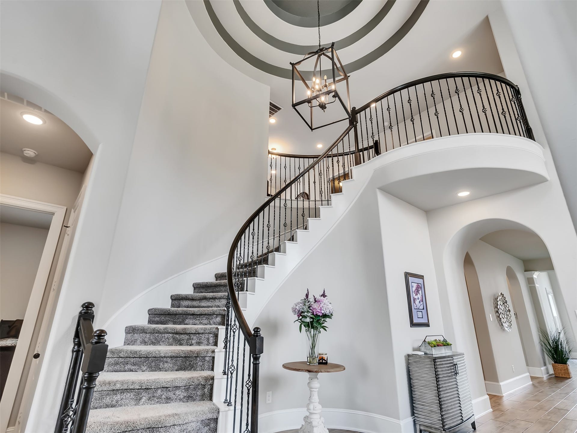 10302 Muir Peak Drive, Rosharon, TX 77583 A curved staircase with iron railings, a high ceiling with a stylish light fixture, and neutral tones.