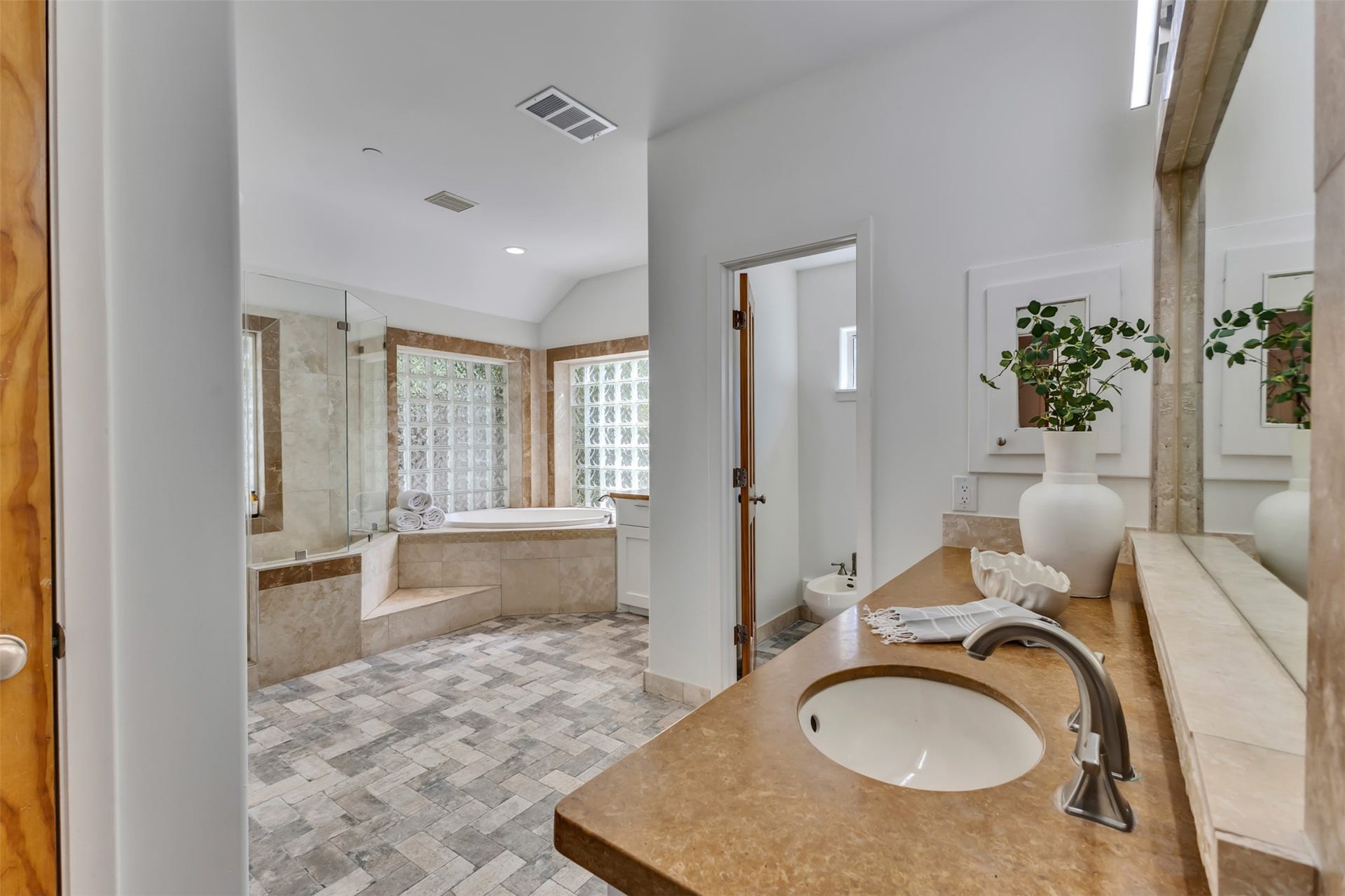 Elegant primary bath complete with dual vanities, a soaking tub, separate large glass shower with a bench, and a private water closet with a bidet.