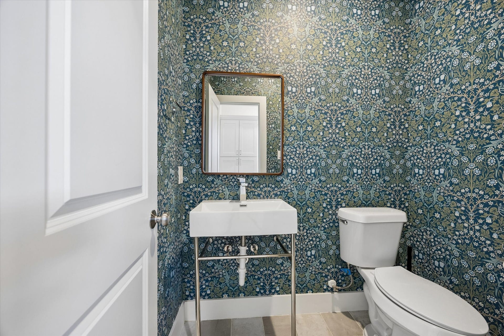 10659 Mayfield Road, Houston, TX 77043 This chic powder room located in the mud room, features a sleek pedestal sink with a modern faucet and a framed mirror. The bold wallpaper creates a bright and inviting space.