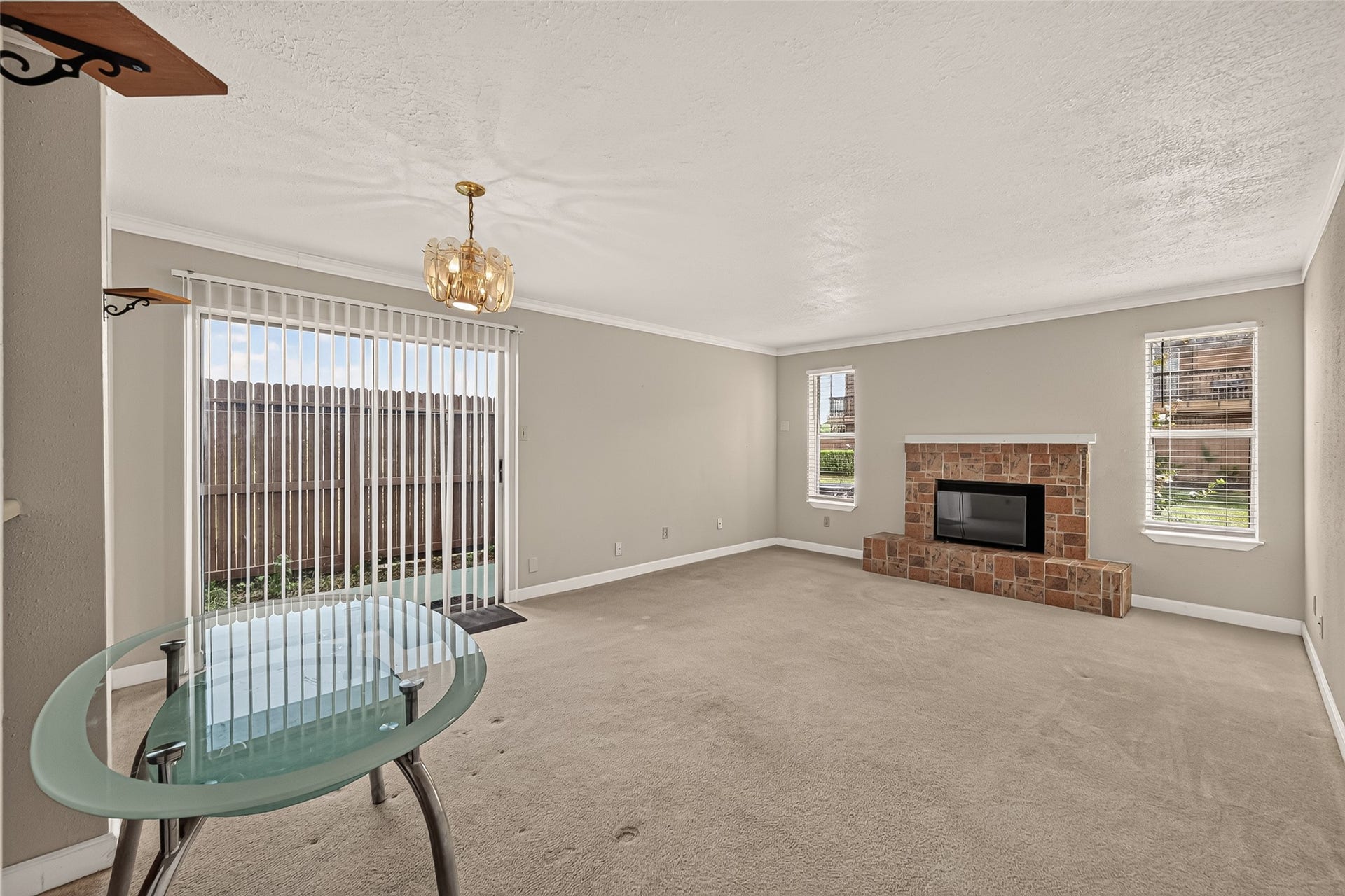 10555 Turtlewood Court, #1006, Houston, TX 77072 Spacious living area with a cozy brick fireplace and ample natural light from large windows and sliding glass doors, providing easy access to the patio.