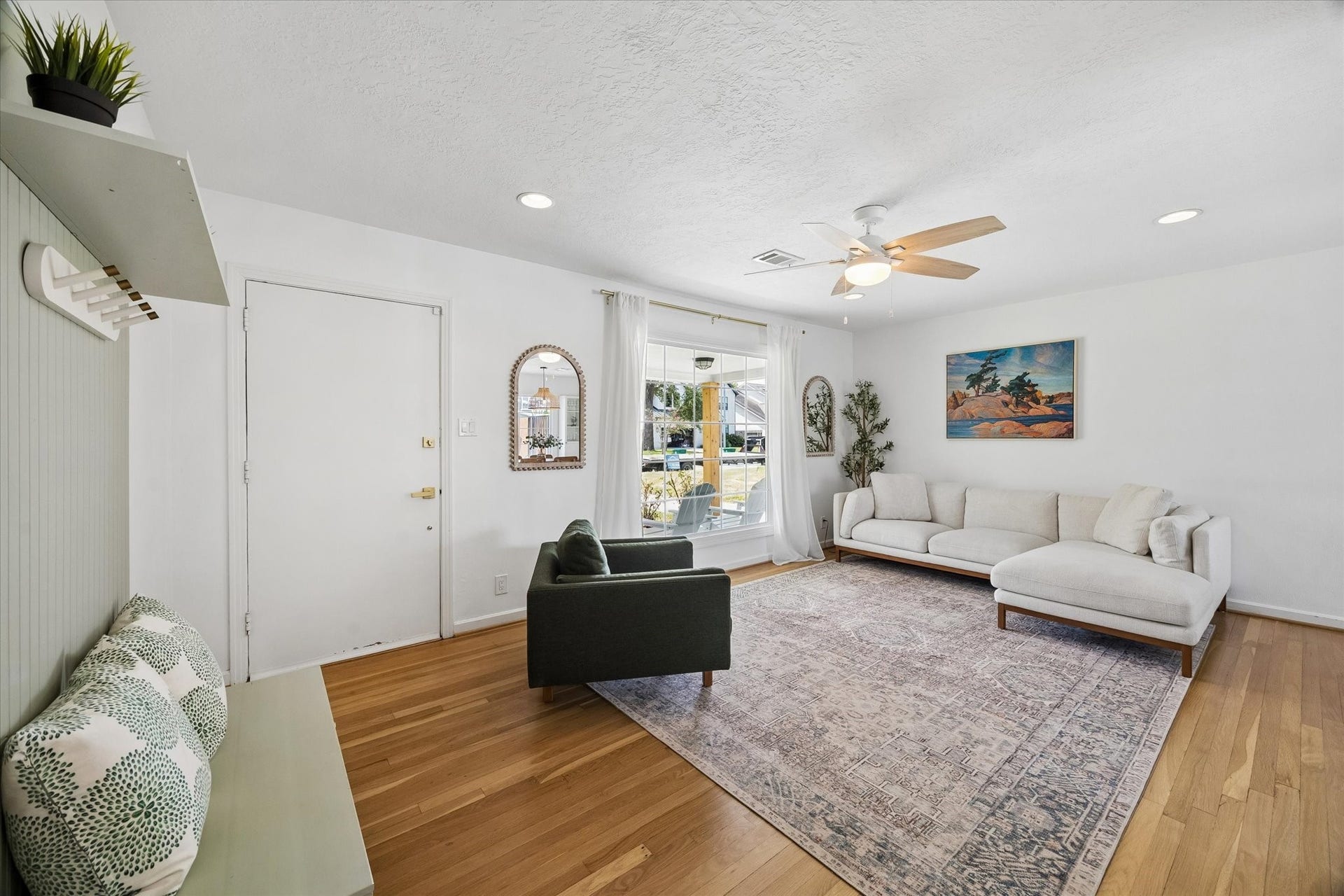 Sun filled living room showcases original hardwood flooring, an oversized picture window, and a comfortable layout with views of the landscaped front yard.