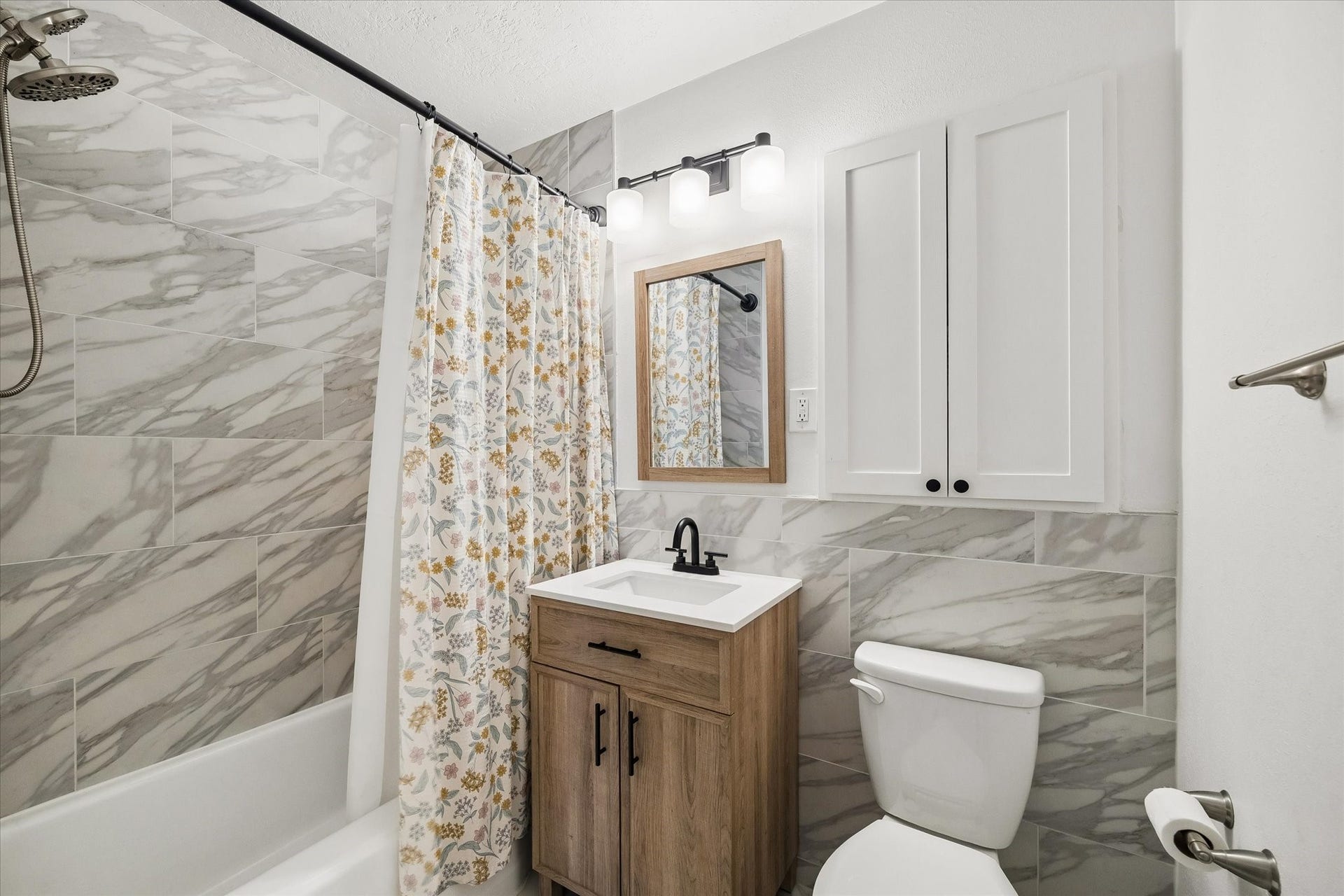 Updated secondary bathroom featuring marble look tile, a modern vanity, black fixtures, and a tub and shower combination.