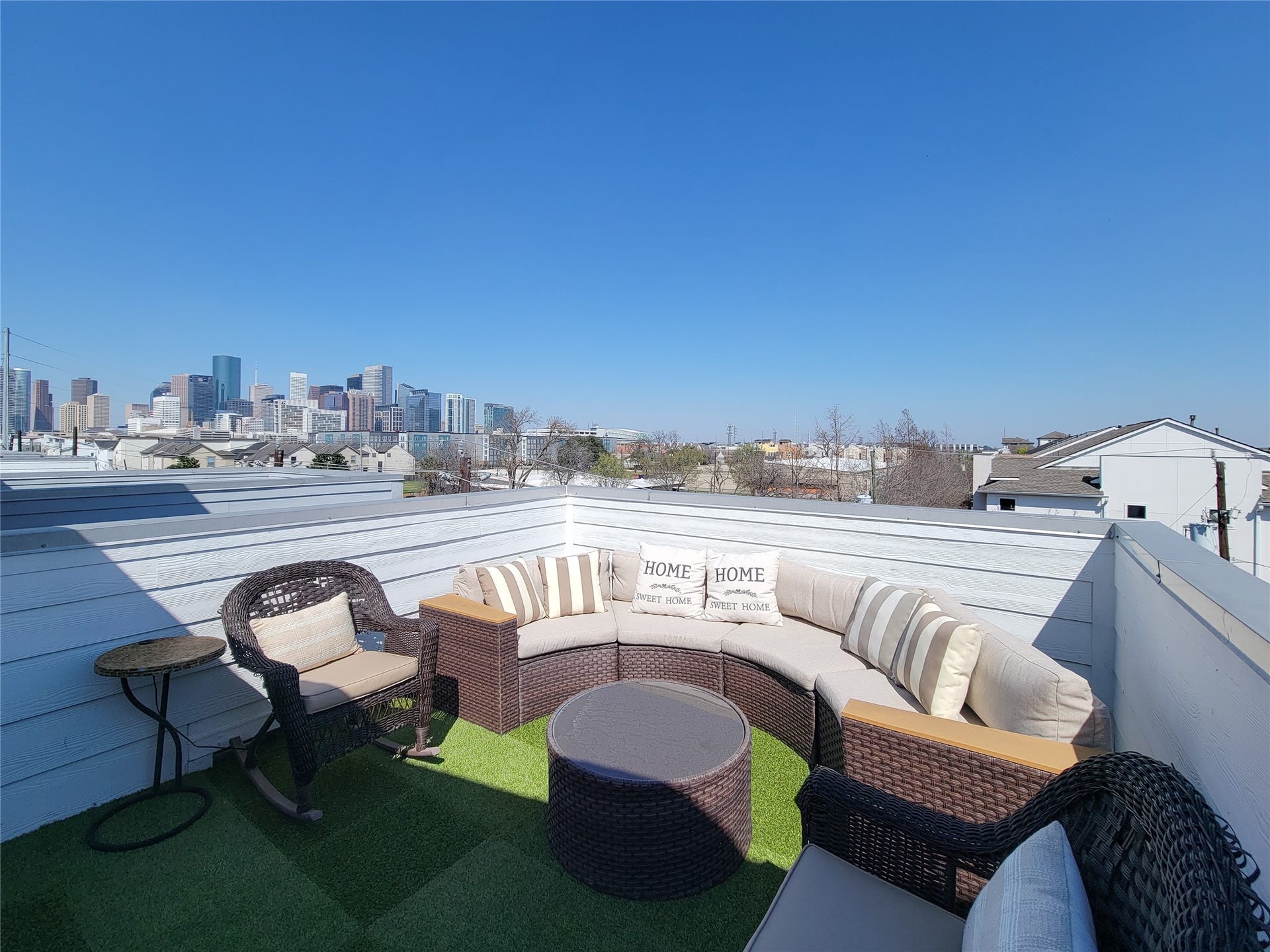 1705 Eado Point Lane, Houston, TX 77003 Welcome to Eado Living! This rooftop patio offers a cozy seating area with wicker furniture and a stunning city skyline view, perfect for relaxation and entertaining.