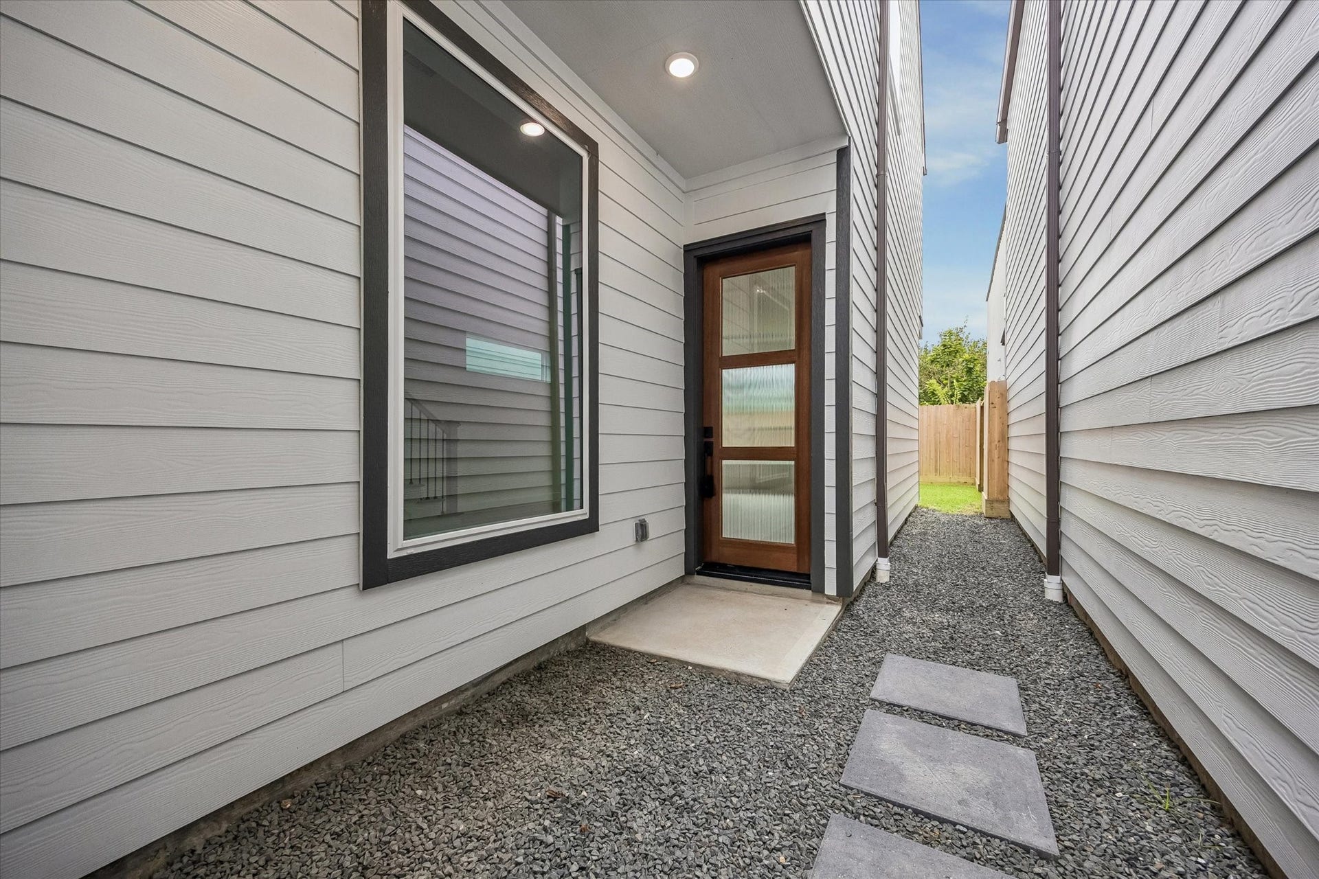 5339 Larkin Street, Houston, TX 77007 Modern side entrance with sleek wood and glass door, framed by clean white siding, leading to a private backyard space.