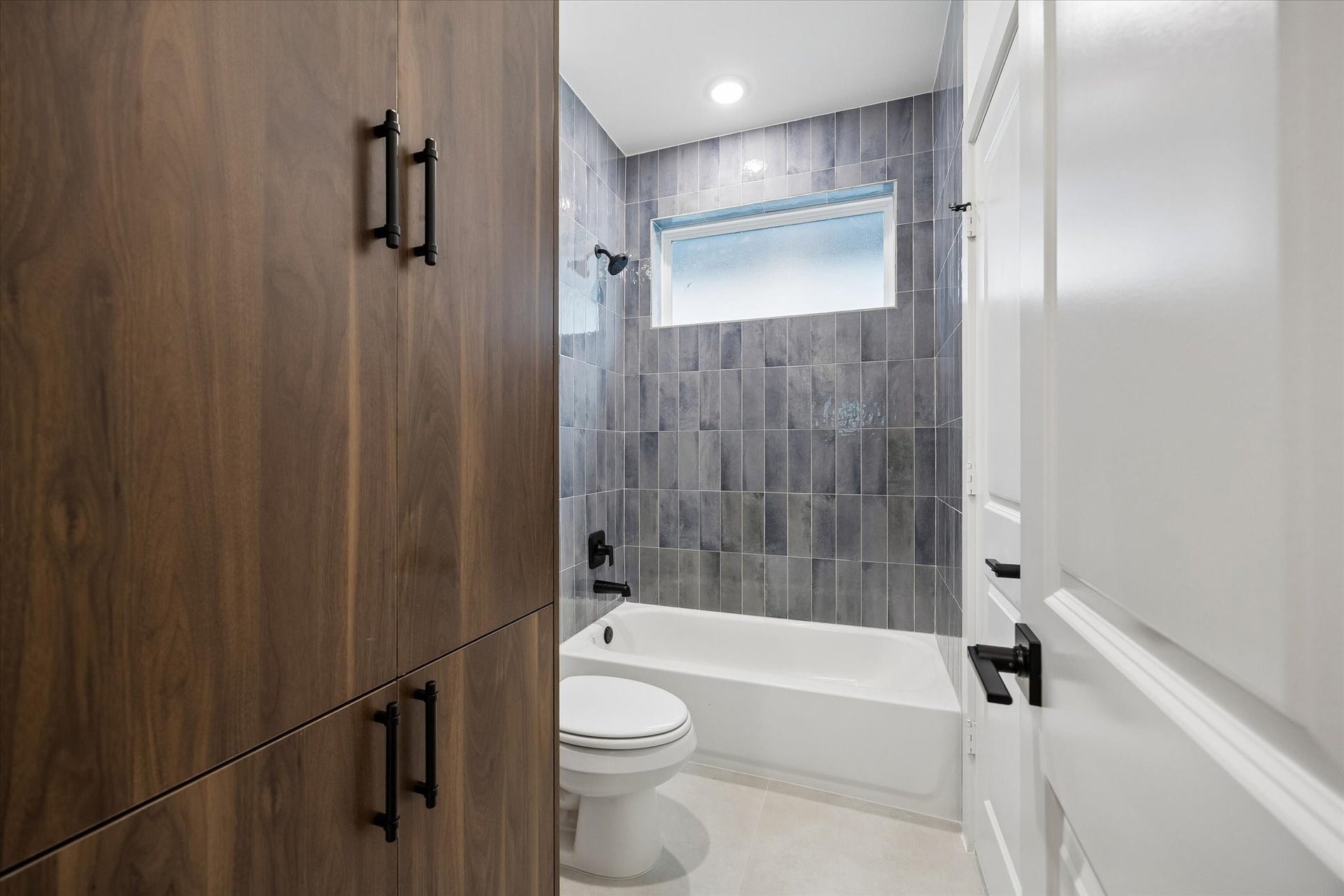 5339 Larkin Street, Houston, TX 77007 Stylish bathroom featuring modern grey tile, a sleek bathtub-shower combo, and ample wooden cabinetry for storage.