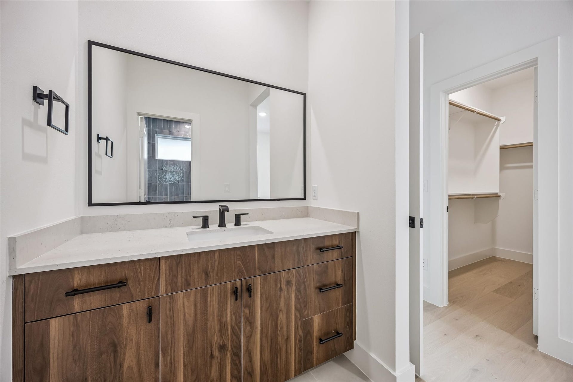 5339 Larkin Street, Houston, TX 77007 Modern bathroom featuring a sleek vanity with wood cabinetry, a large mirror, and black fixtures, leading to a spacious walk-in closet with ample shelving.