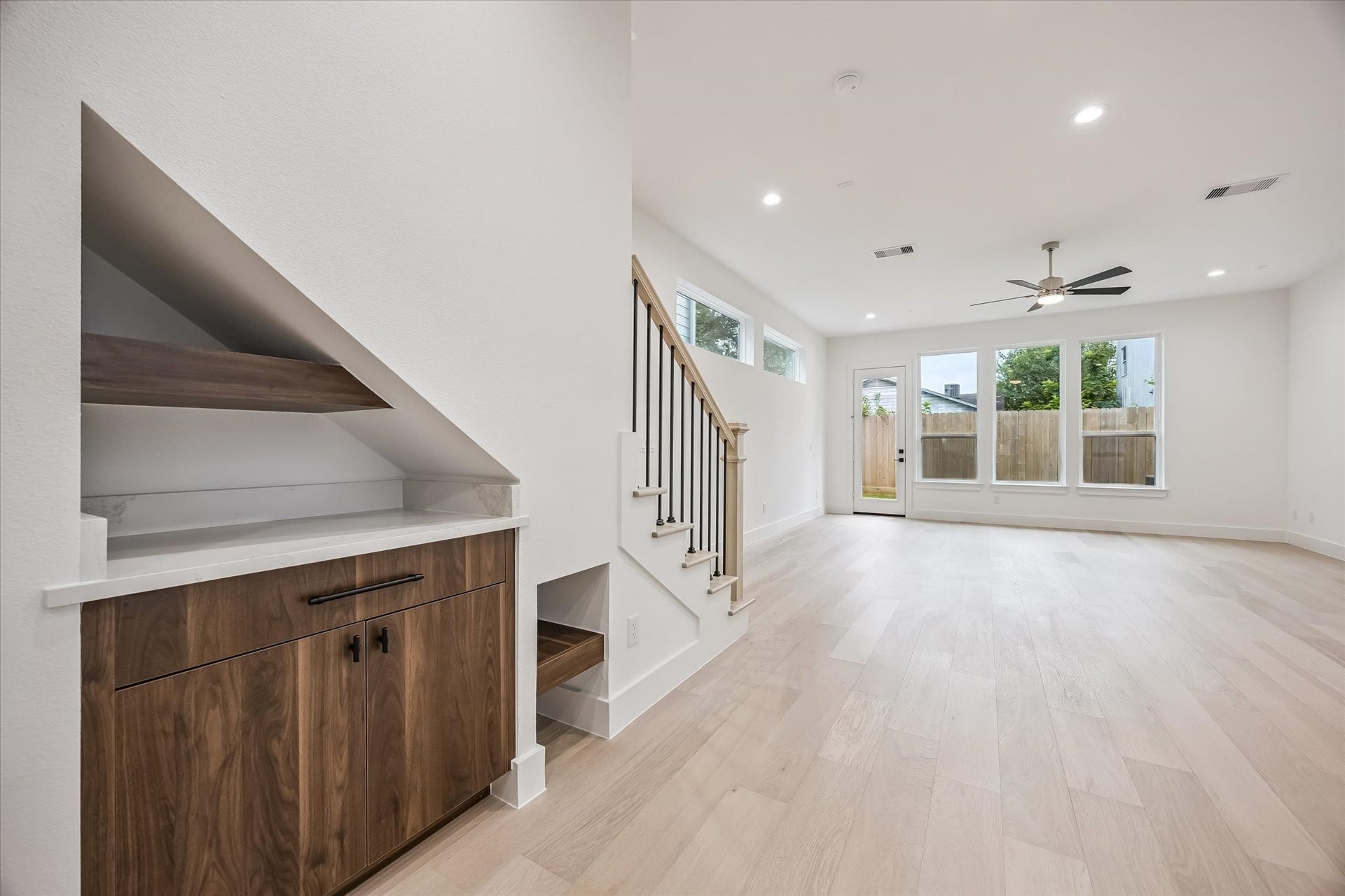 5339 Larkin Street, Houston, TX 77007 Bright and spacious living area featuring sleek hardwood floors, a modern ceiling fan, and large windows that flood the room with natural light, complemented by a stylish built-in cabinet under the staircase.