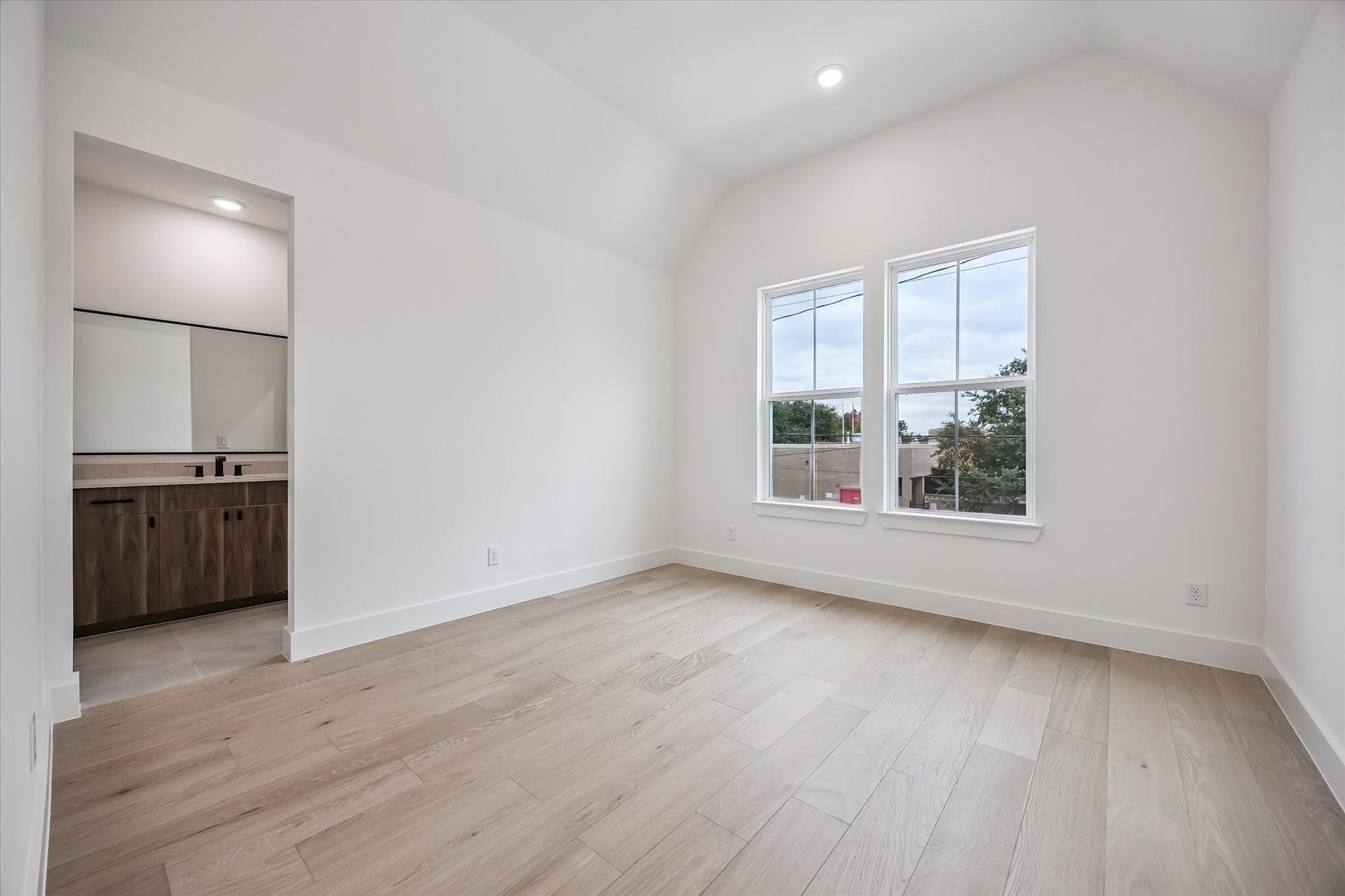 5339 Larkin Street, Houston, TX 77007 Bright and airy bedroom with vaulted ceilings, wood flooring, and large windows, leading into a modern en-suite bathroom with sleek cabinetry.