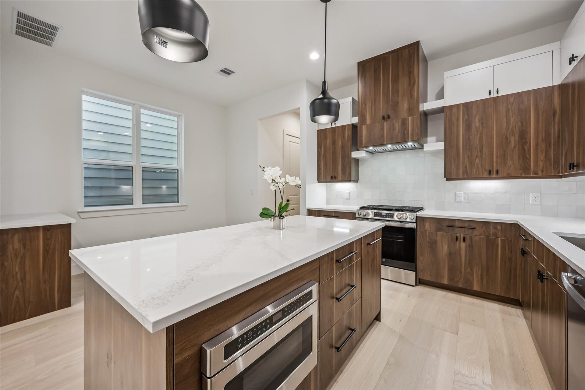 5339 Larkin Street, Houston, TX 77007 Stunning modern kitchen with sleek wood cabinetry, a spacious island with a built-in microwave, and elegant pendant lighting, creating a perfect blend of style and functionality.