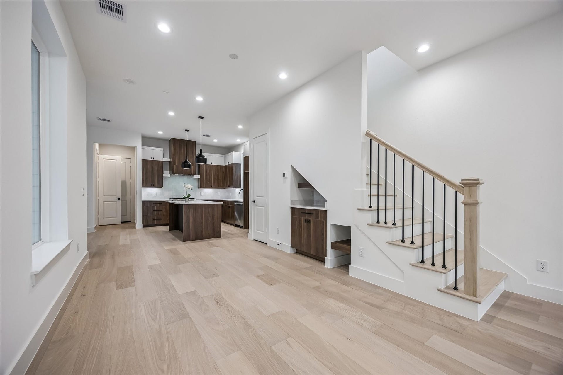 5339 Larkin Street, Houston, TX 77007 Modern open-concept living area featuring sleek wood flooring, a stylish kitchen with pendant lighting, and a contemporary staircase with black iron railings.