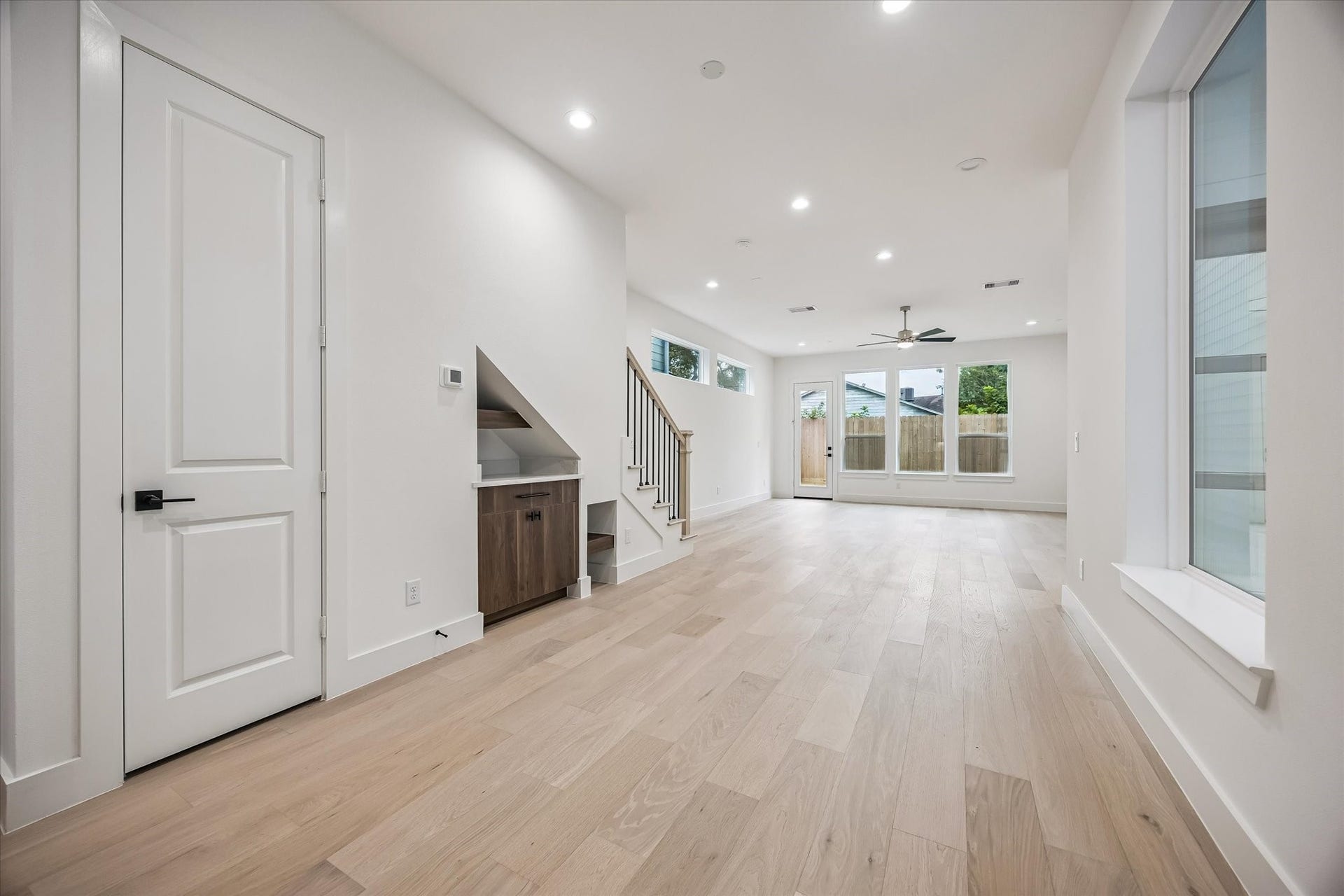 5339 Larkin Street, Houston, TX 77007 Spacious and bright living area with light wood floors, recessed lighting, and large windows leading to a backyard. Features a modern staircase and convenient built-in storage under the stairs.