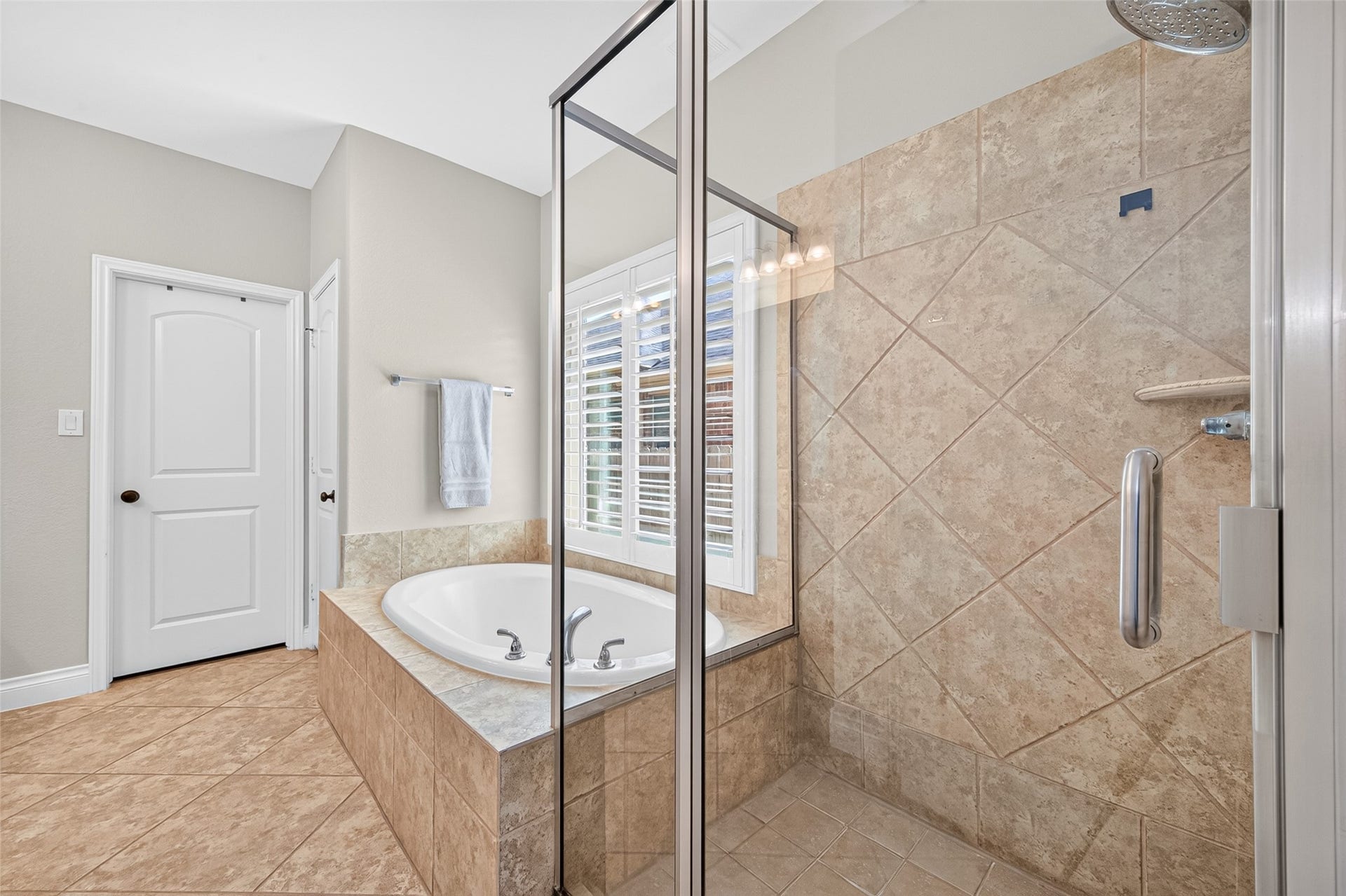 6710 Aqua Falls, Missouri City, TX 77459 Primary bathroom featuring a luxurious soaking tub, glass-enclosed shower, dual sink vanity, and elegant tile flooring, illuminated by ample natural light through large windows.