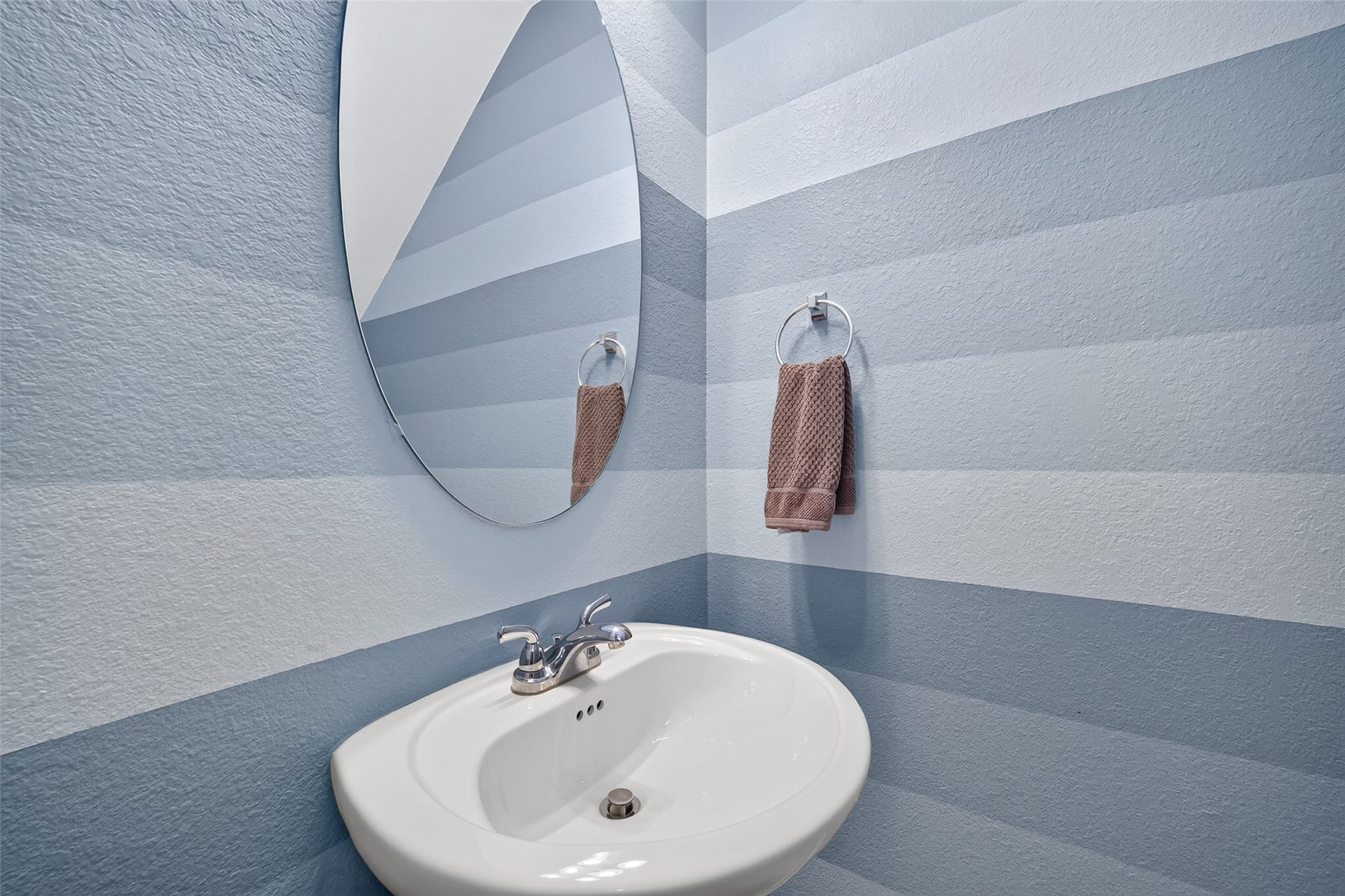 6710 Aqua Falls, Missouri City, TX 77459 Powder room with modern striped walls, an elegant oval mirror, and a sleek pedestal sink.