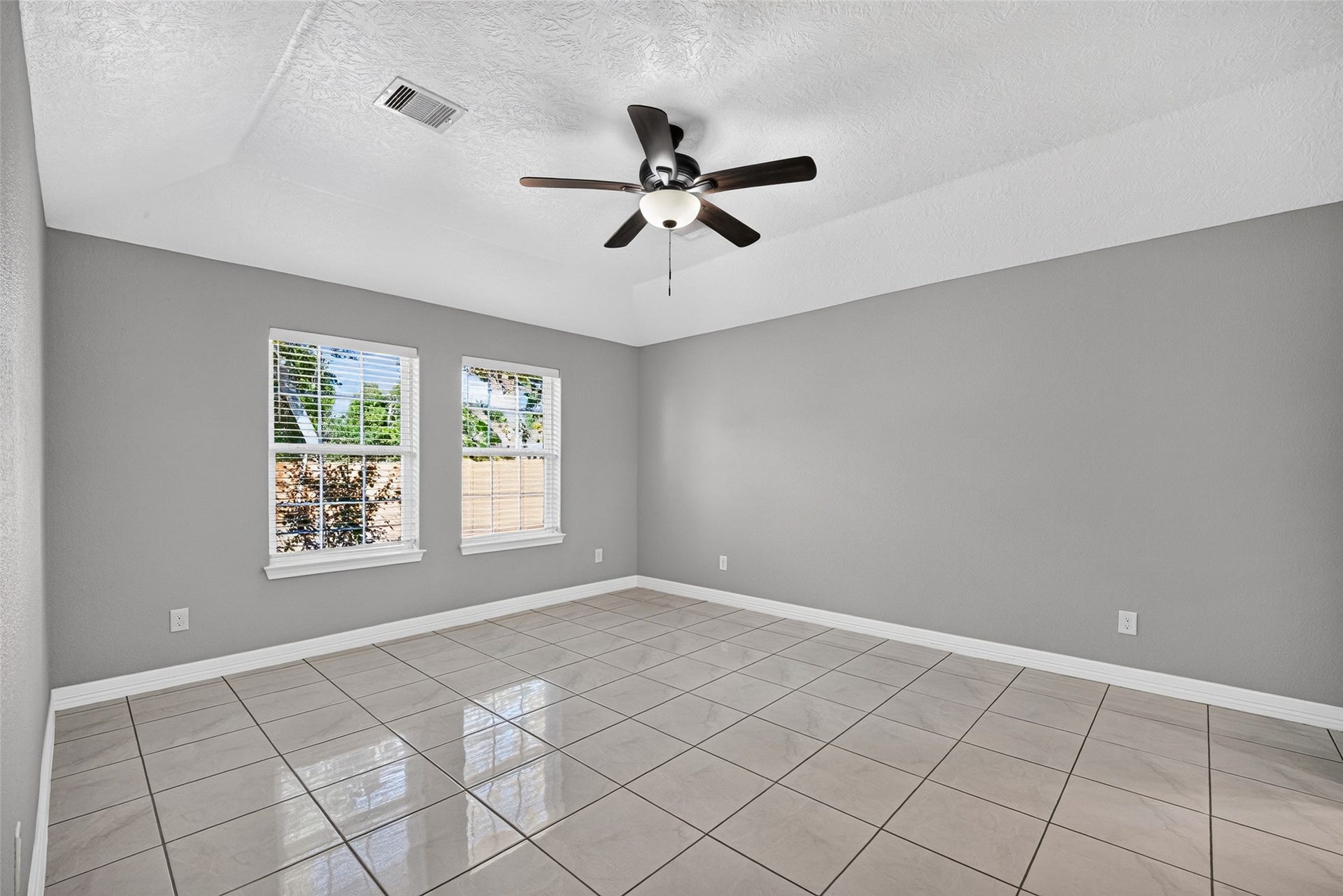 803 Avenue K, South Houston, TX 77587 Spacious primary bedroom with sleek tile flooring, neutral gray walls, and ample natural light from two large windows, complemented by a modern ceiling fan and en suite.