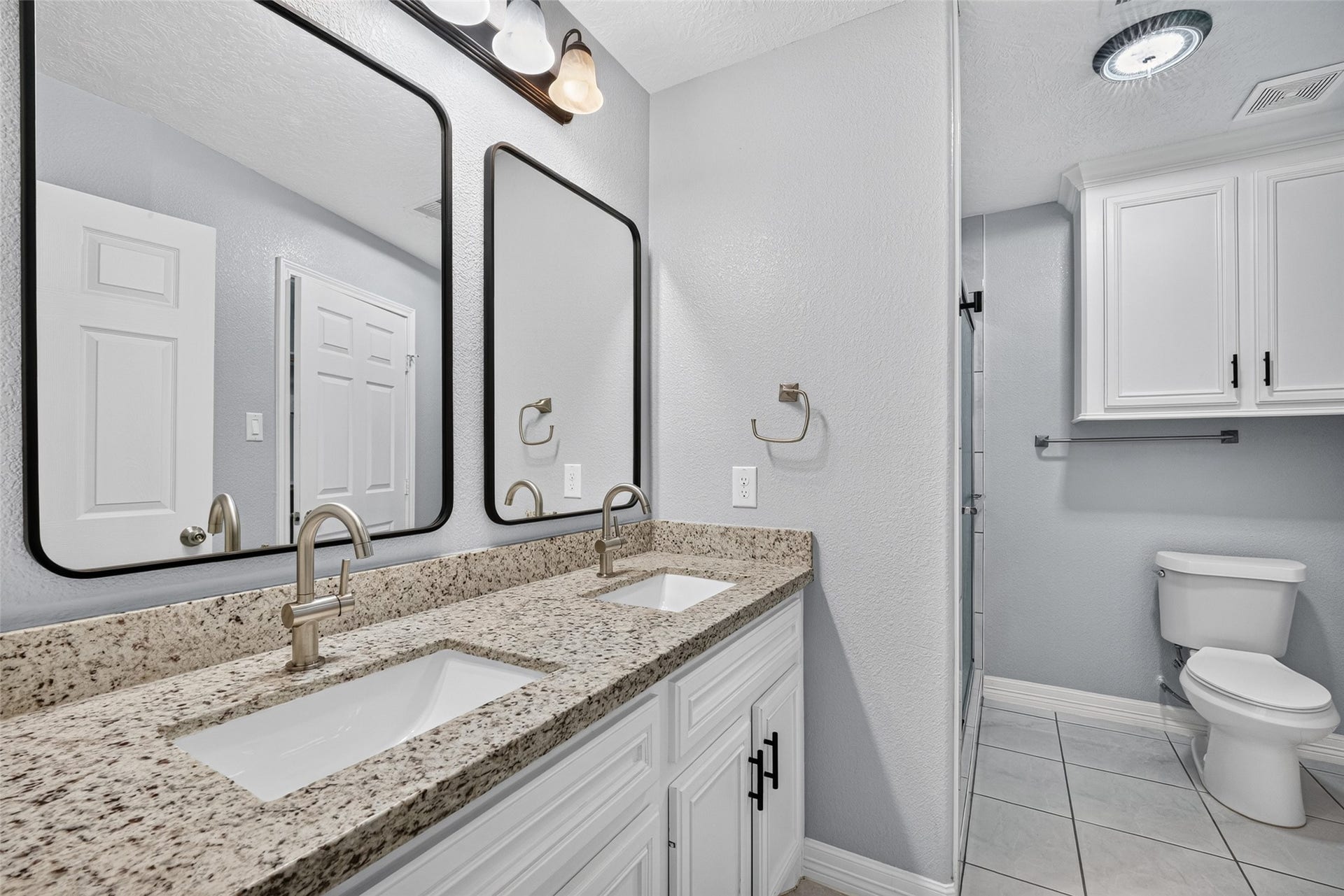 803 Avenue K, South Houston, TX 77587 Elegant en suite featuring a dual-sink vanity with granite countertops, modern fixtures, and ample storage, complemented by soft gray walls and tile flooring.