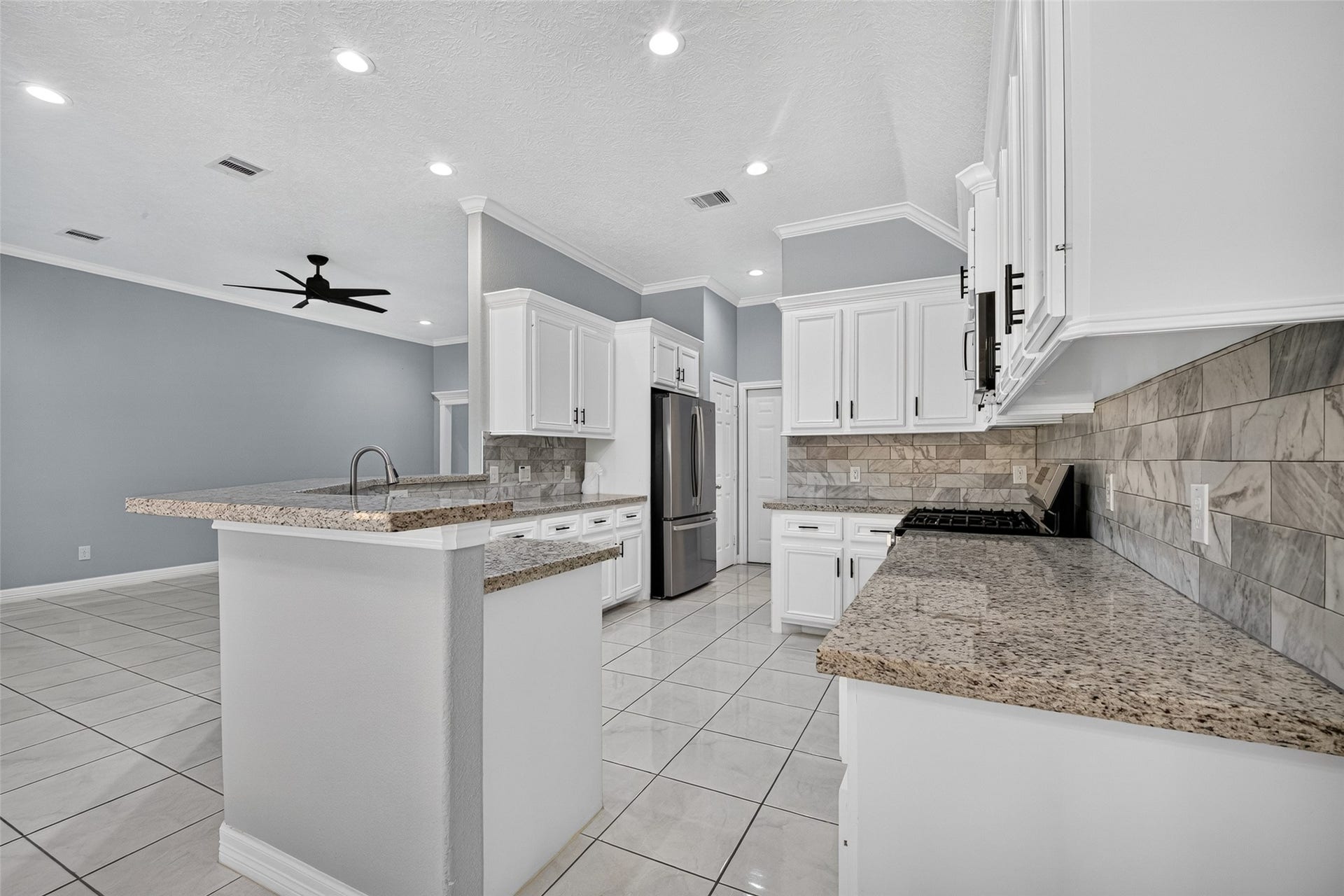 803 Avenue K, South Houston, TX 77587 Spacious kitchen with modern stainless steel appliances, elegant granite countertops, and sleek white cabinetry, seamlessly flowing into an open living area with high ceilings and recessed lighting.