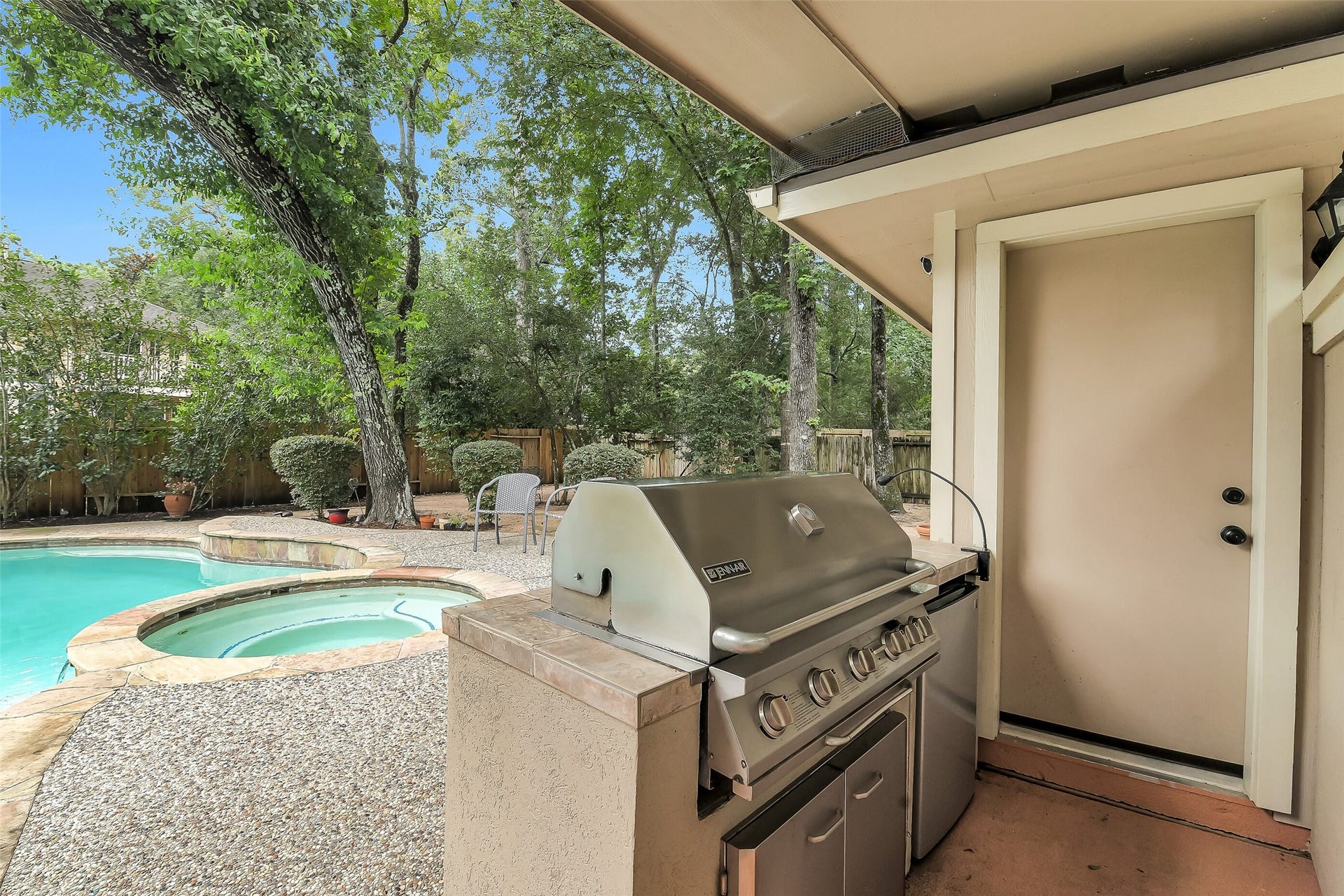 7 Larkspur Trail, The Woodlands, TX 77382 Enjoy outdoor living with a built-in grill overlooking a sparkling pool and spa, surrounded by lush greenery for a private retreat.