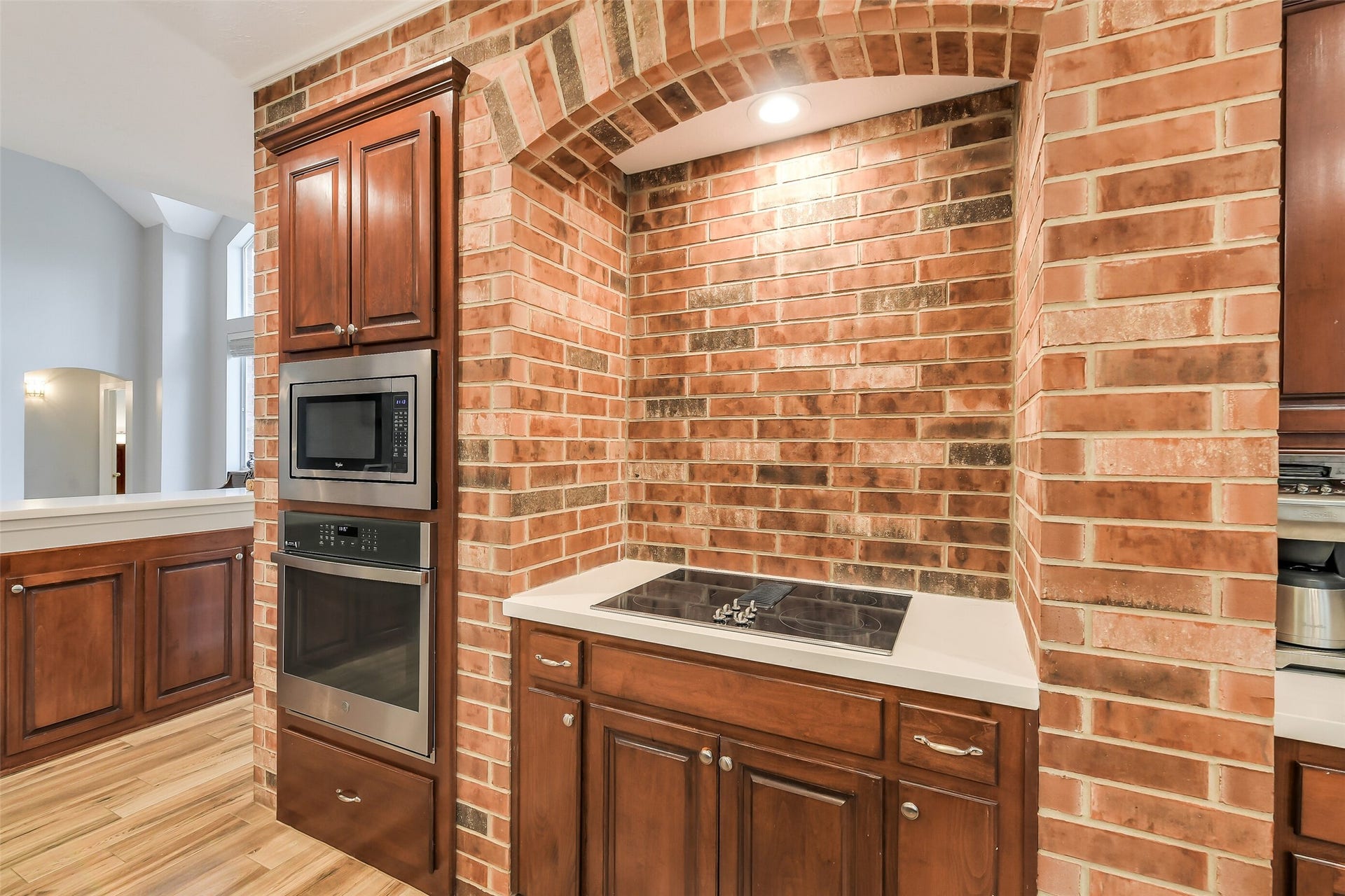 7 Larkspur Trail, The Woodlands, TX 77382 Elegant kitchen nook features a built-in cooktop set against a charming brick archway, complemented by rich wooden cabinetry and stainless steel appliances.