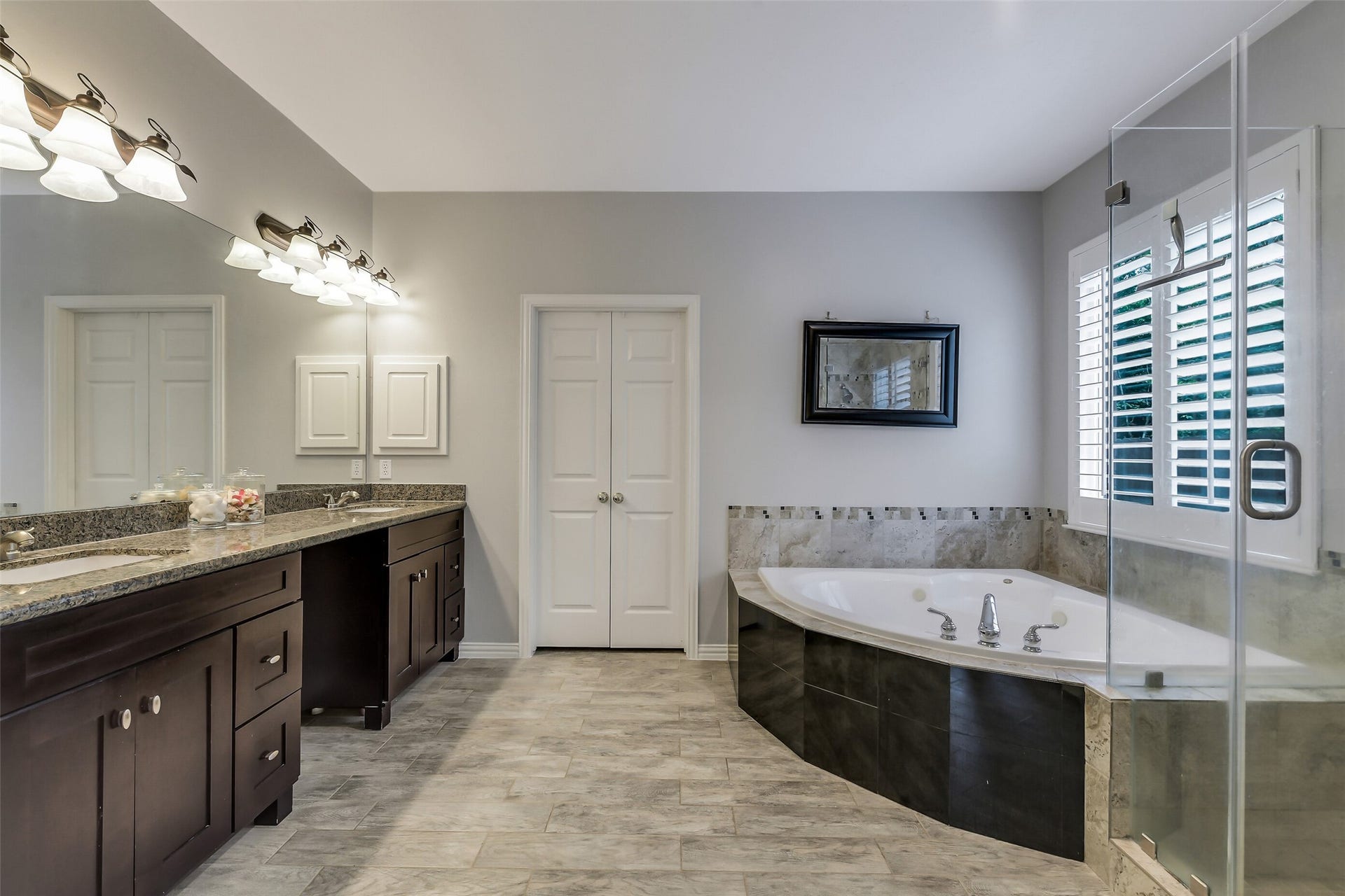 7 Larkspur Trail, The Woodlands, TX 77382 Elegant Primary bathroom featuring a spacious dual-sink vanity with granite countertops, a luxurious corner bathtub, and a glass-enclosed shower, all enhanced by sleek tile flooring and ample natural light.