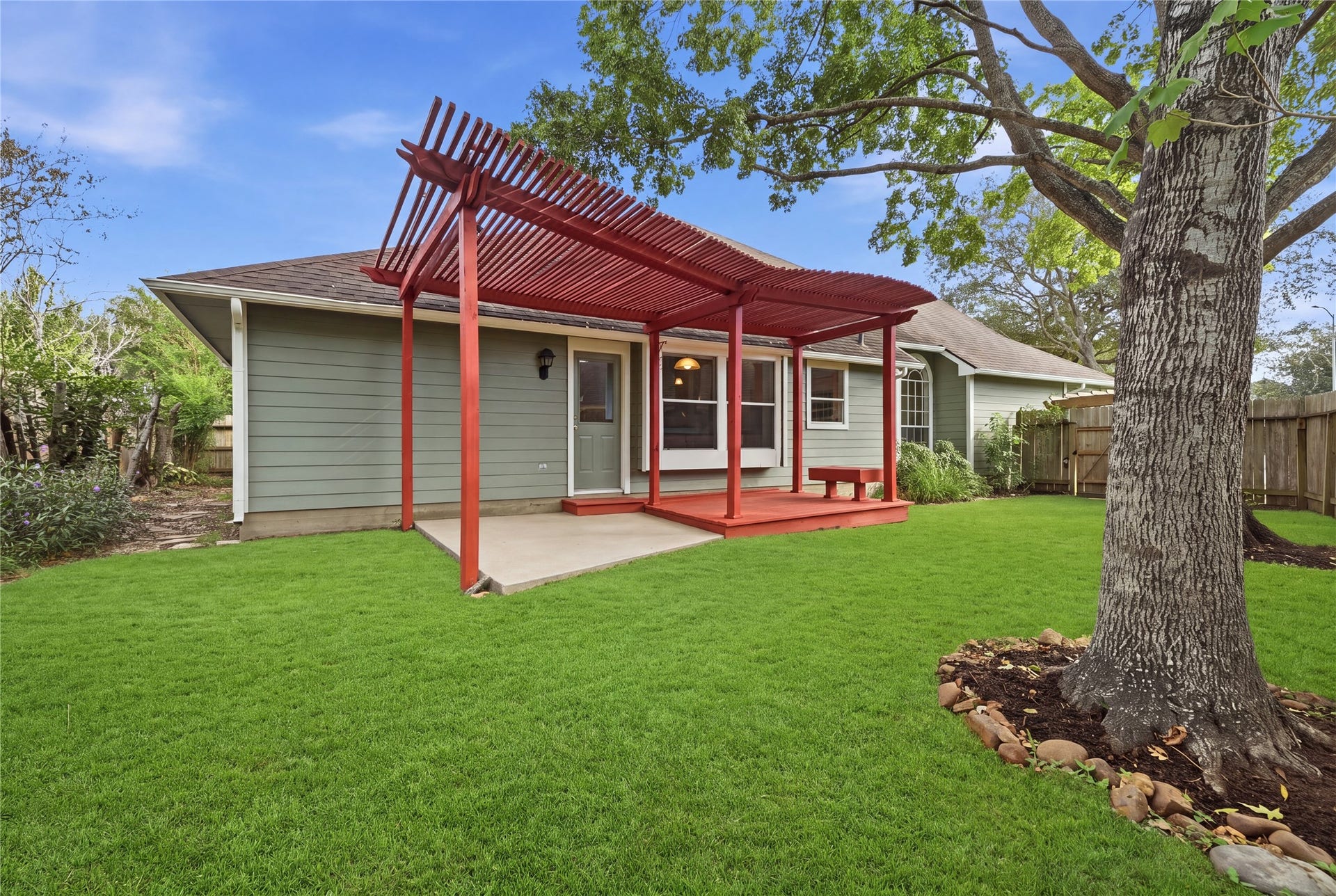 1411 Pebble Banks Lane, Seabrook, TX 77586 Lush fully fenced backyard featuring a vibrant red pergola covered patio deck alongside an open concrete patio pad.